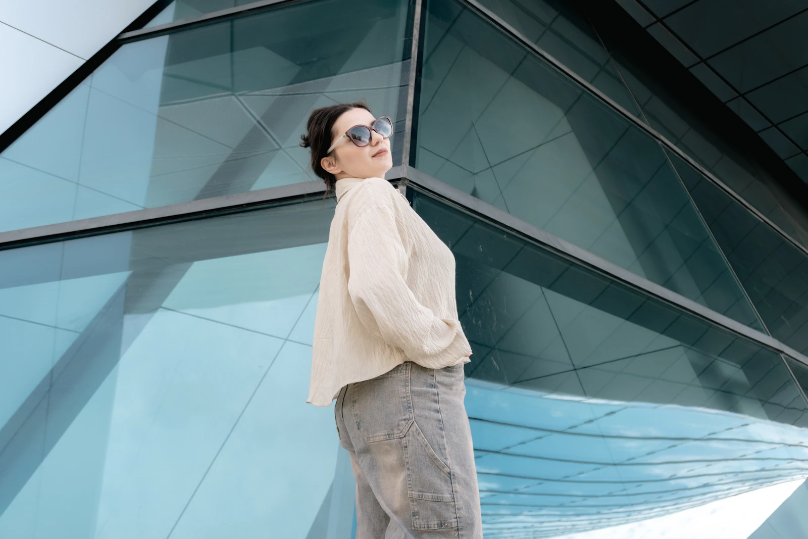 Woman in a cream blouse and wide-leg jeans by a glass facade