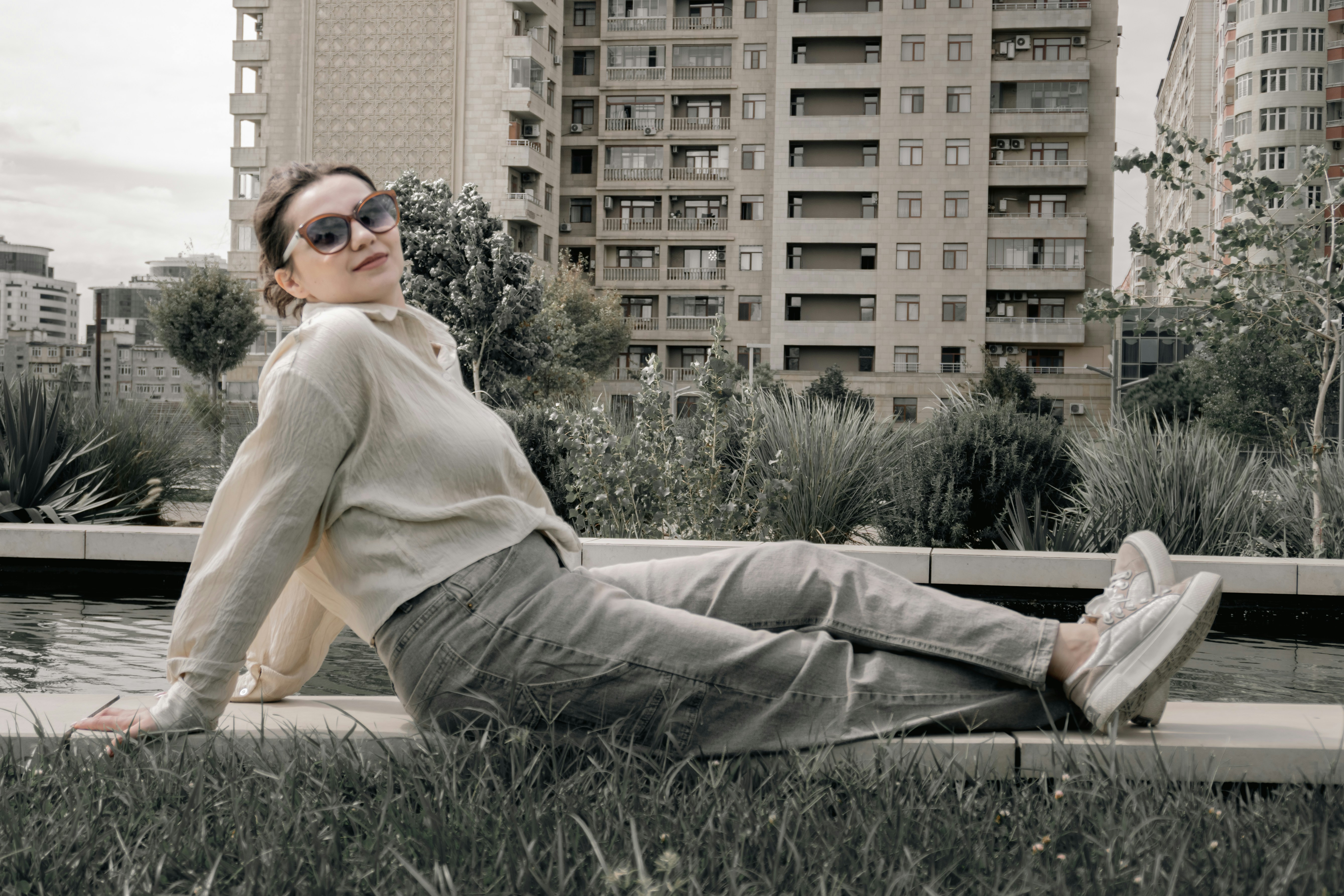 A woman in sunglasses relaxes on a wall near buildings