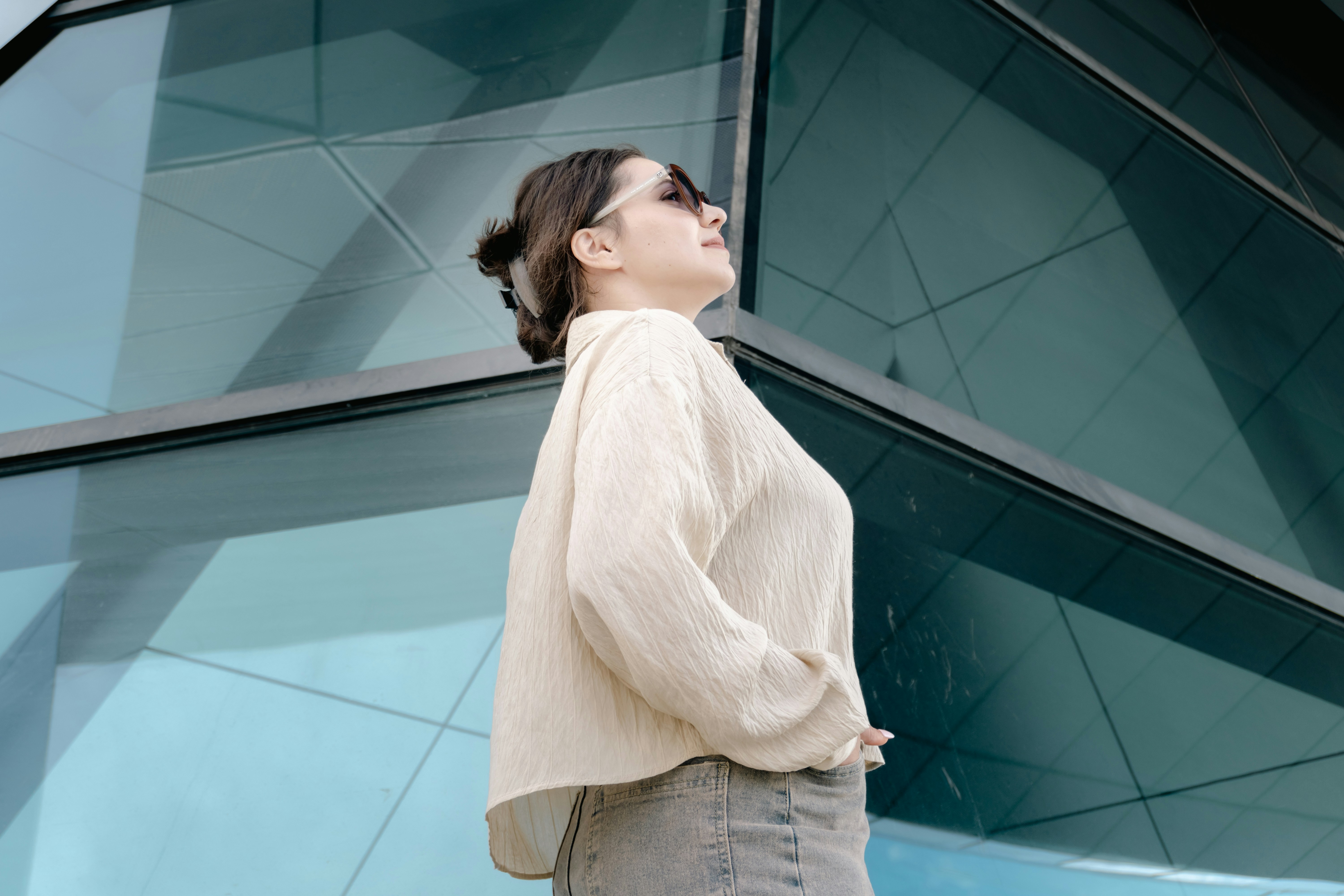 Woman in sunglasses looking up at a modern glass building