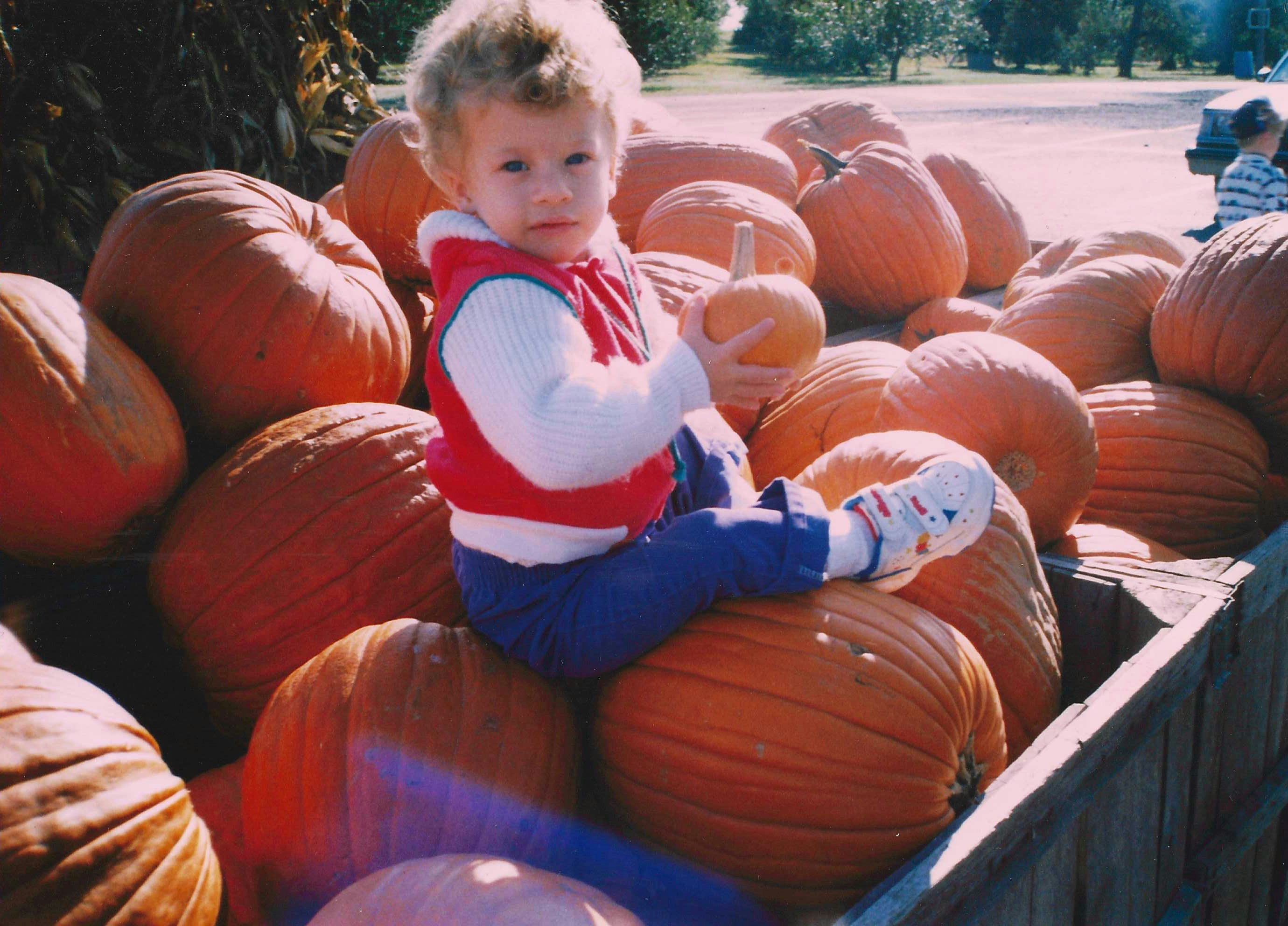 Un jeune enfant est assis sur des citrouilles, tenant une petite.
