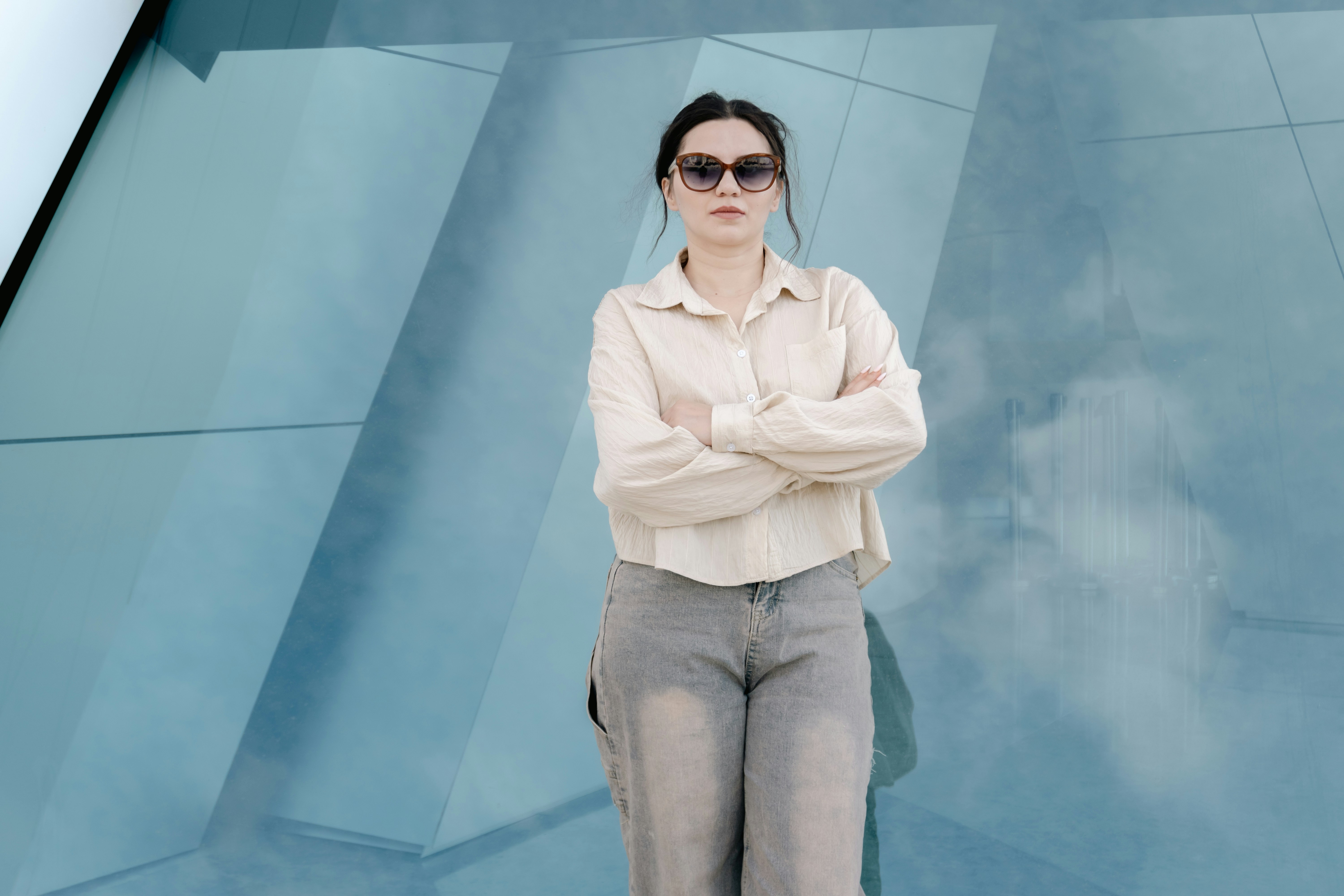 Woman in sunglasses with arms crossed against blue geometric wall