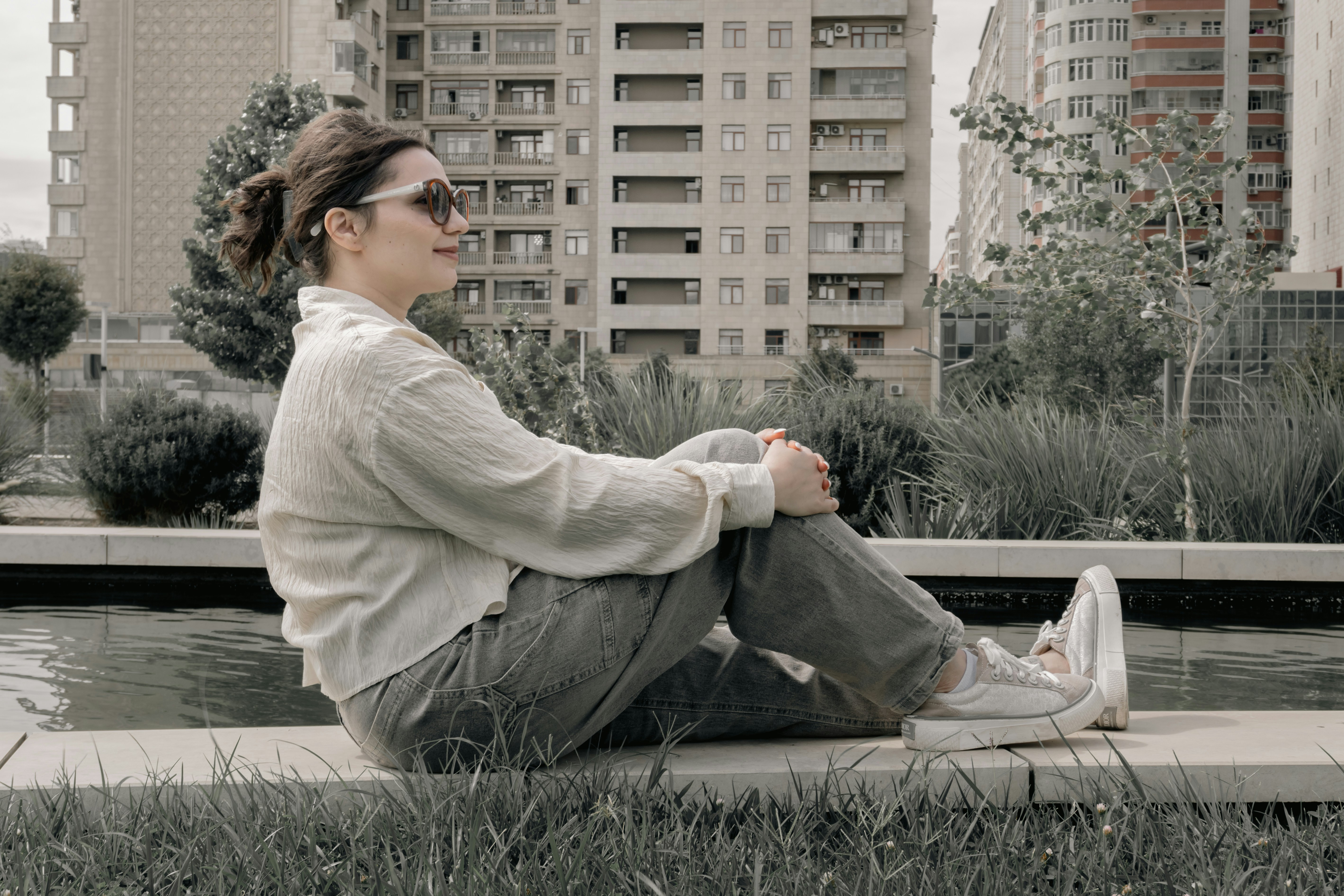 A woman relaxes outdoors by water in an urban setting.