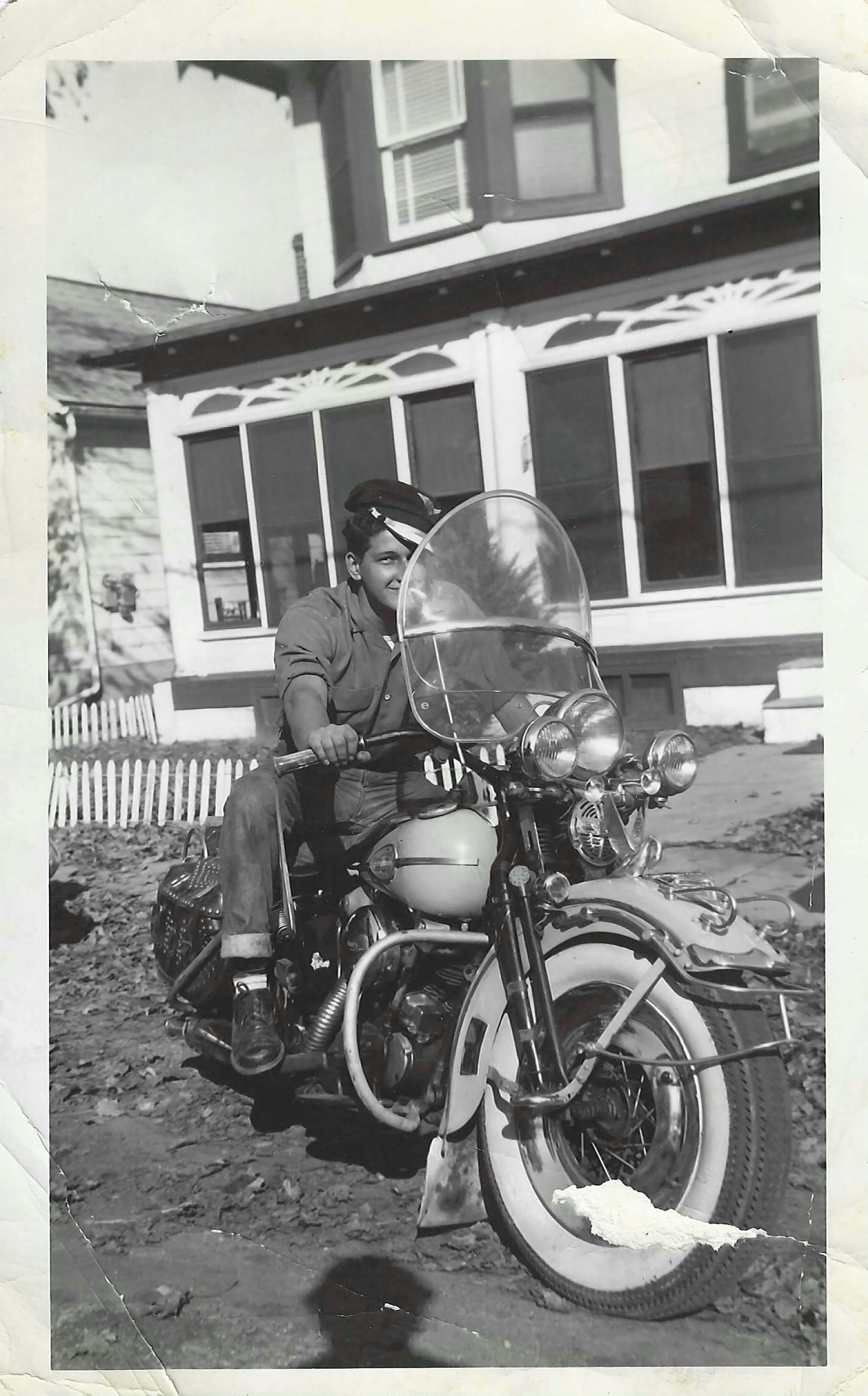 Un homme souriant sur une moto classique devant une maison.