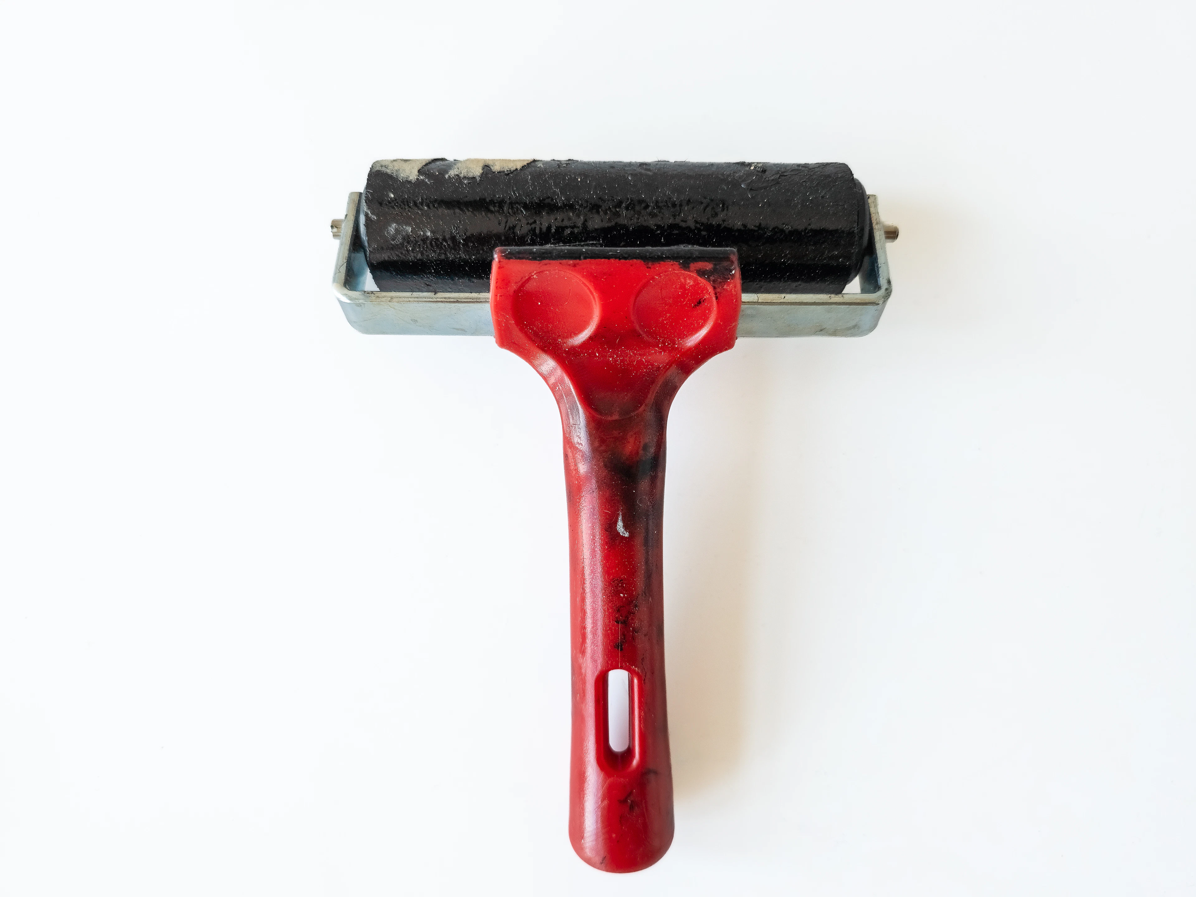 A red-handled printmaking brayer with an inked black roller on white paper.