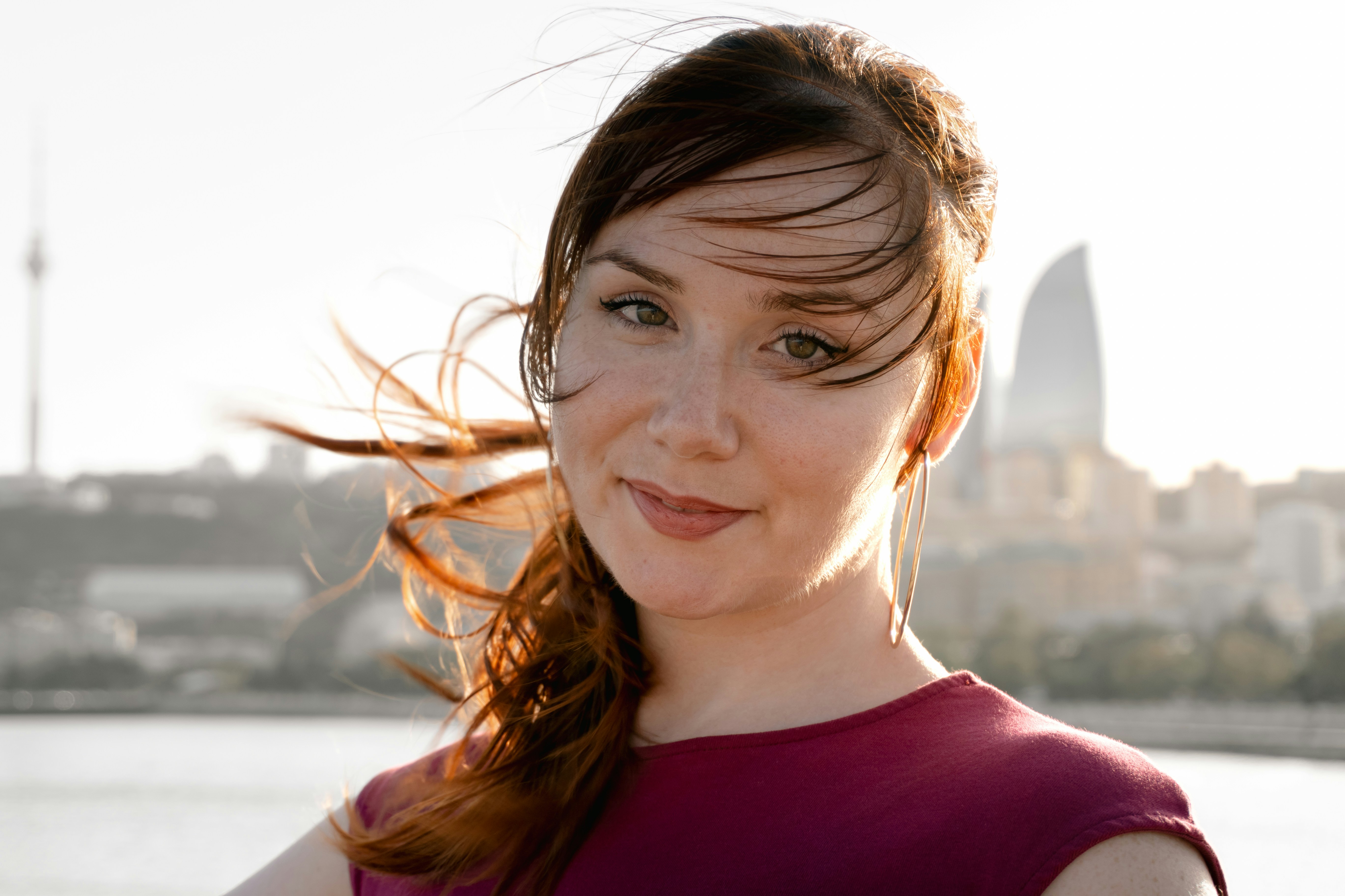 Young woman with windblown hair smiles against a city skyline.