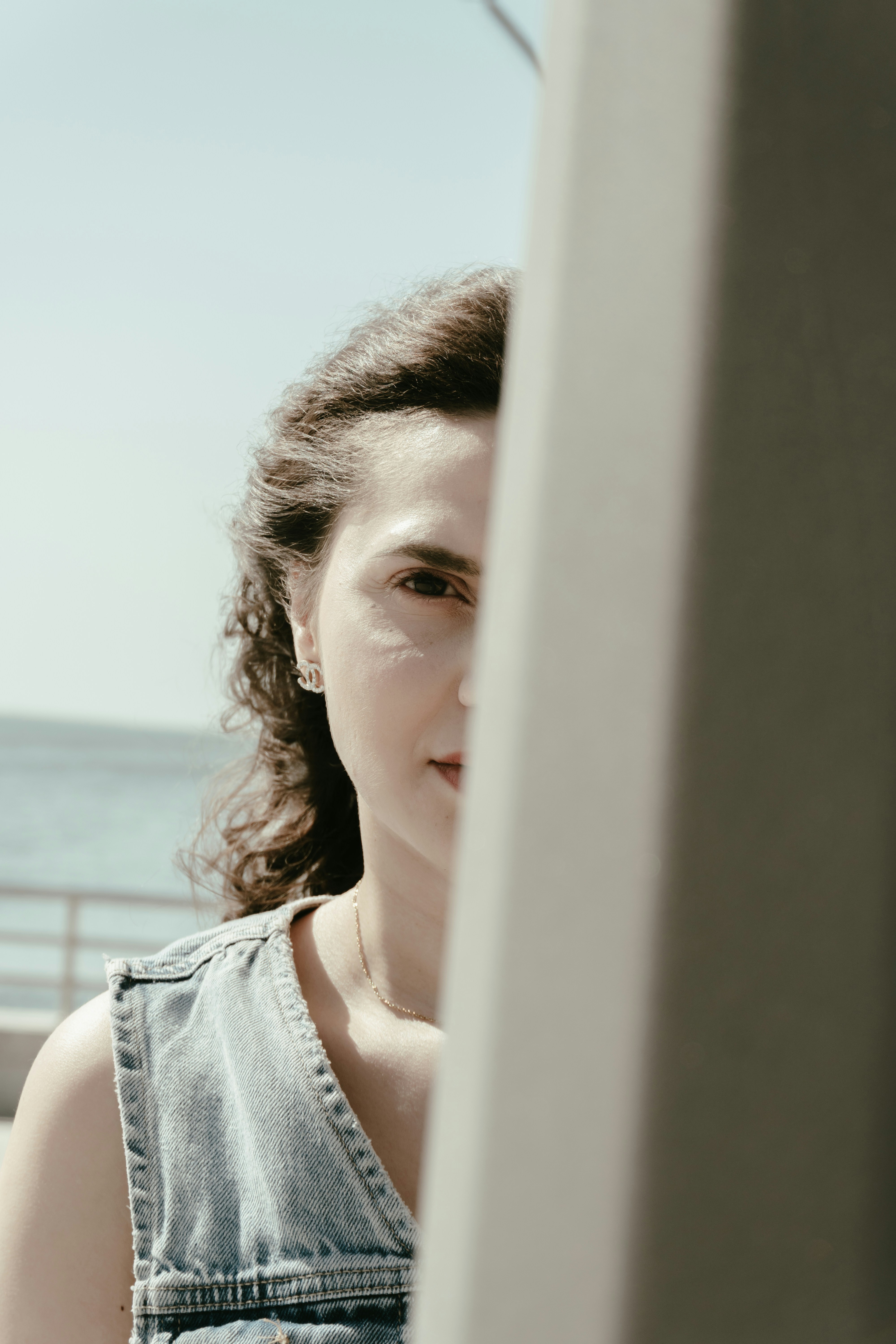 Woman with curly hair peeking, ocean visible in background.