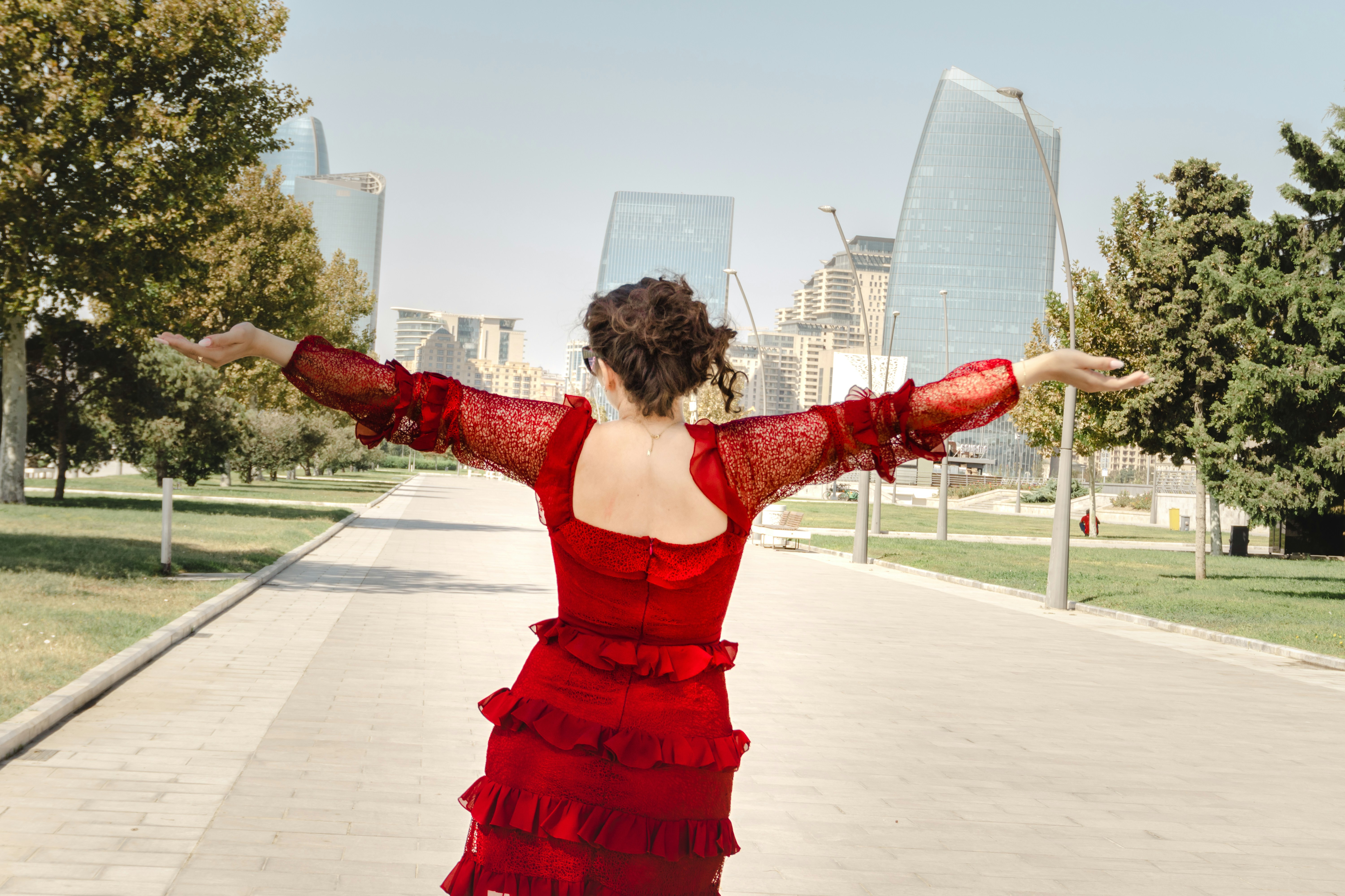 Woman in red dress with arms open facing modern city