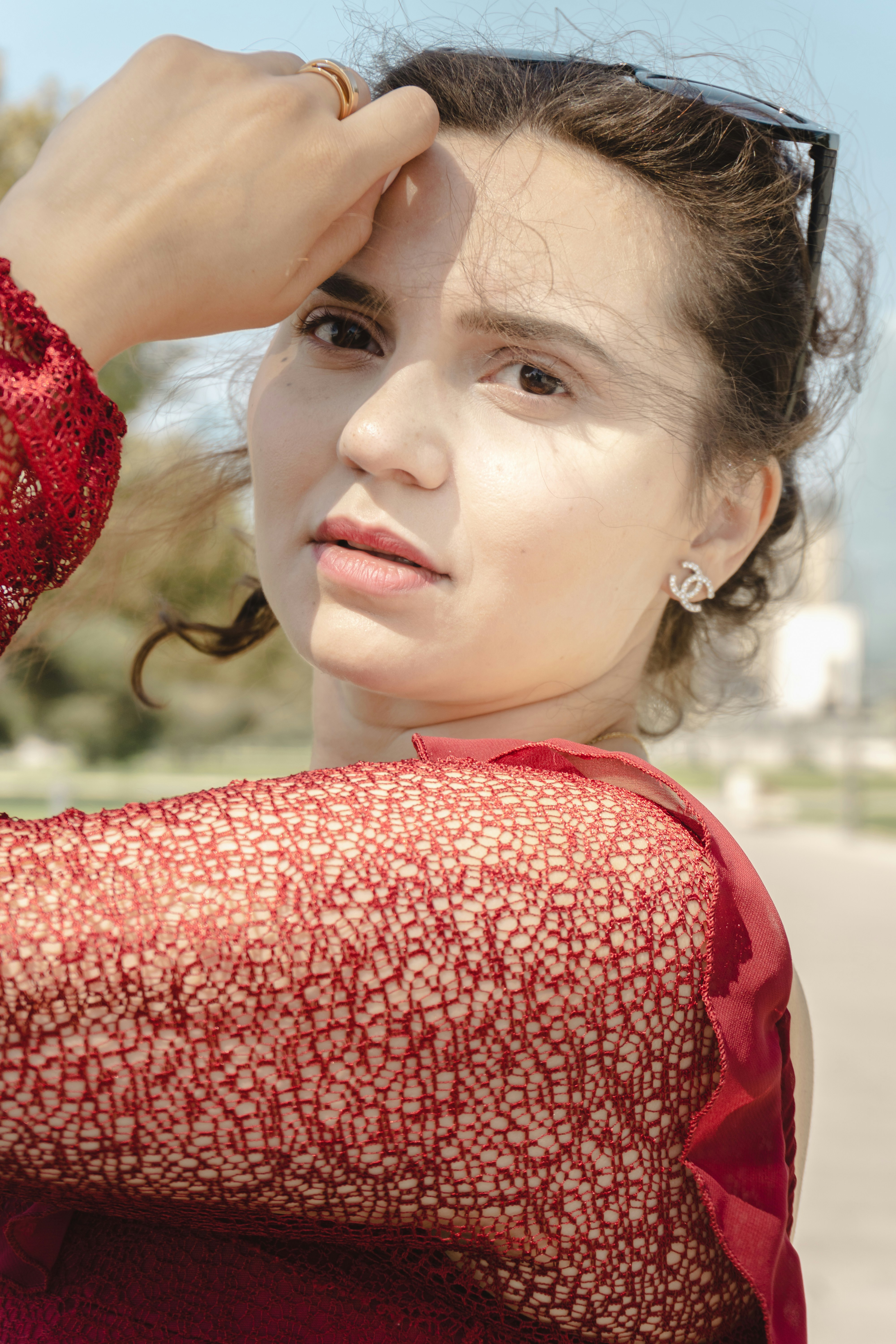 Woman in red lace top with hand on forehead outdoors