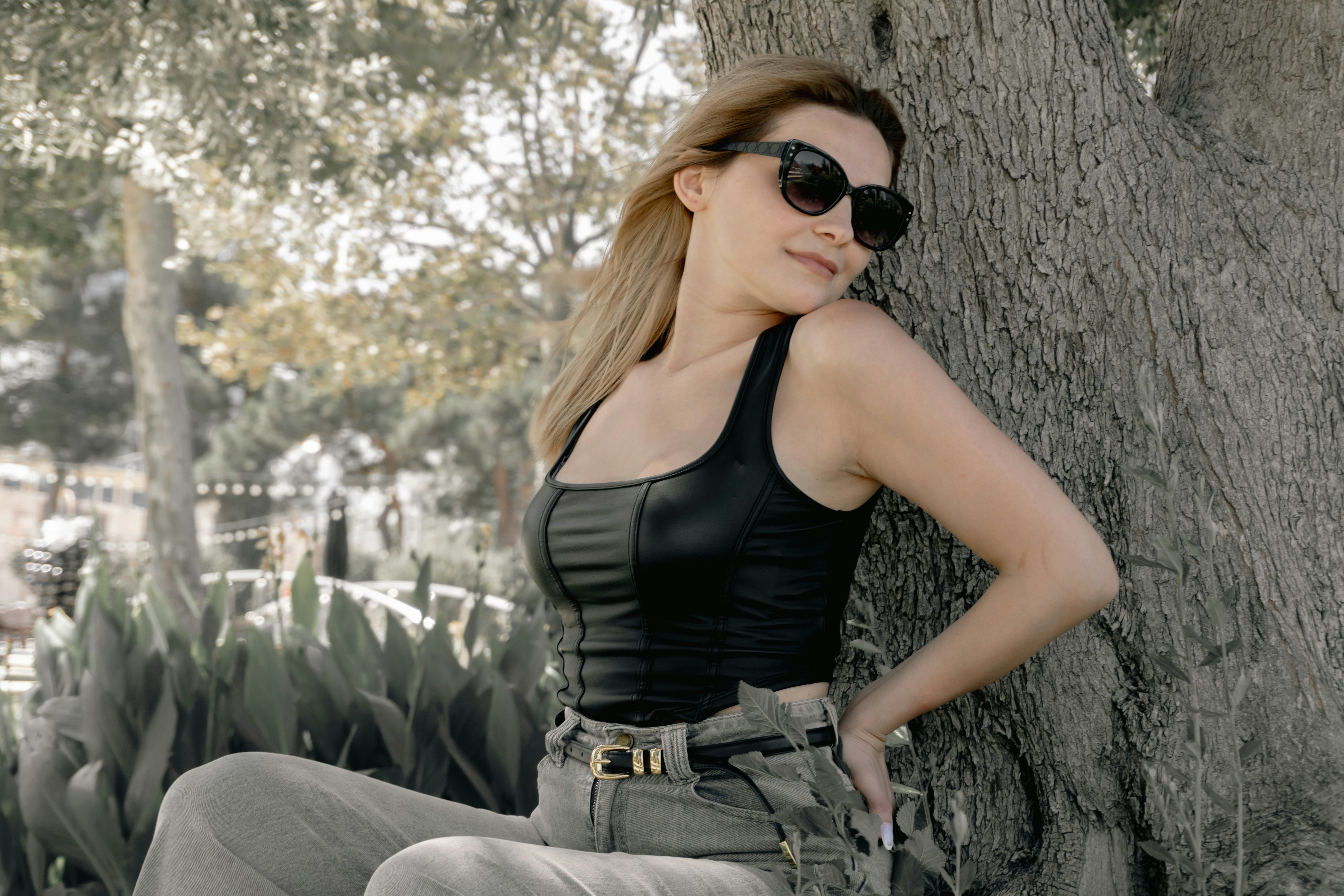 A woman with sunglasses sits leaning against a tree.