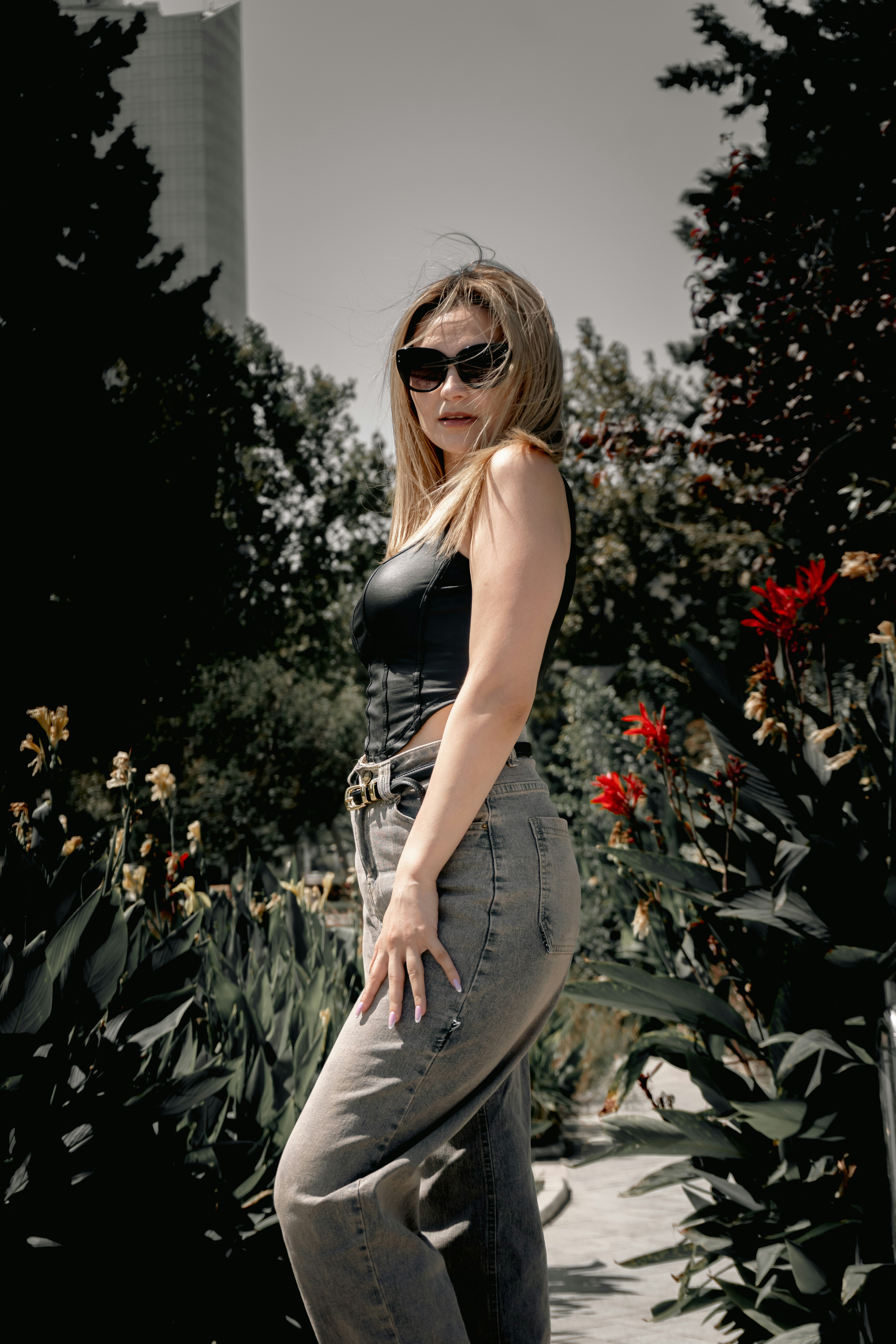 Stylish woman in sunglasses and jeans standing in a garden