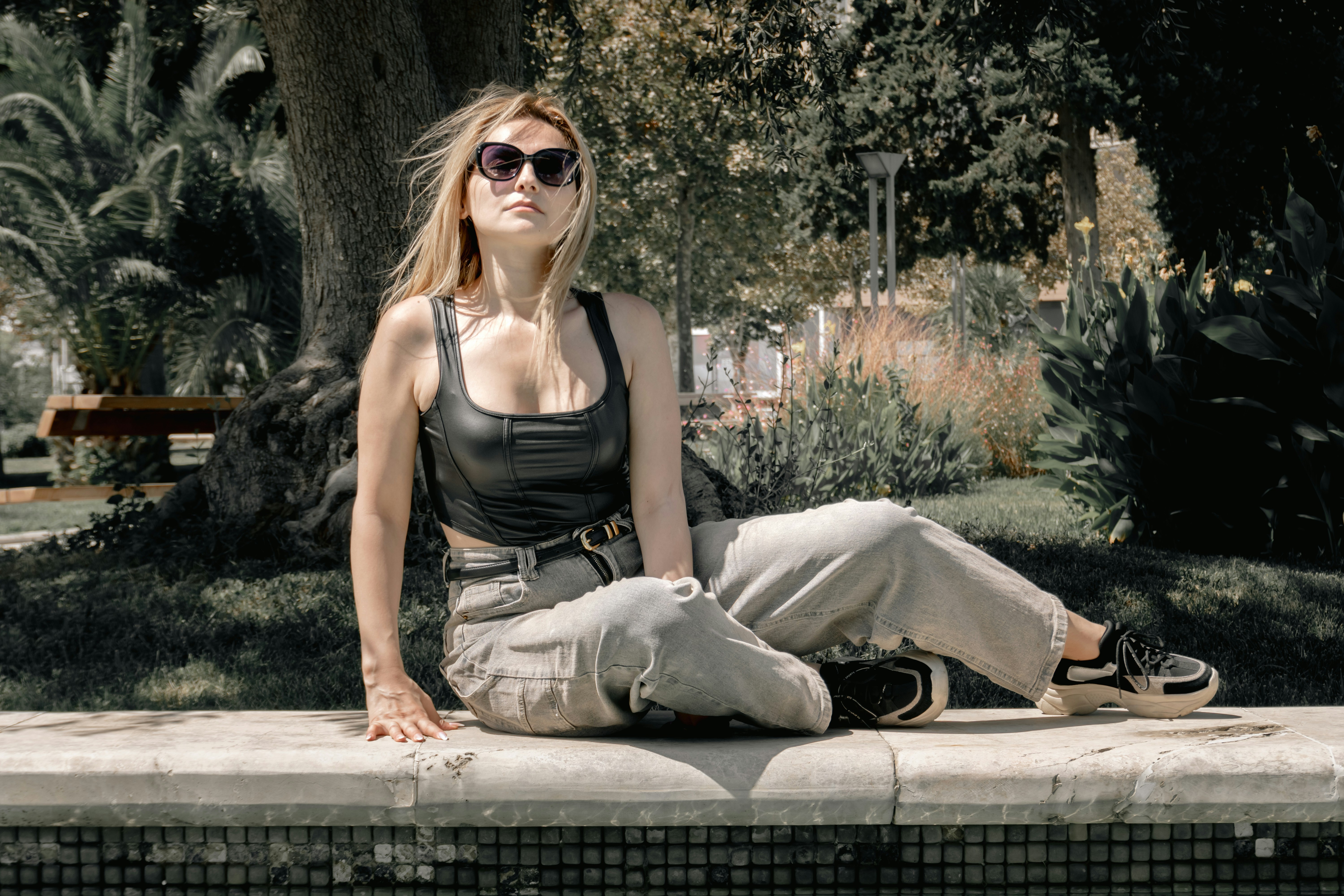 Woman wearing sunglasses sitting on a stone ledge outdoors.
