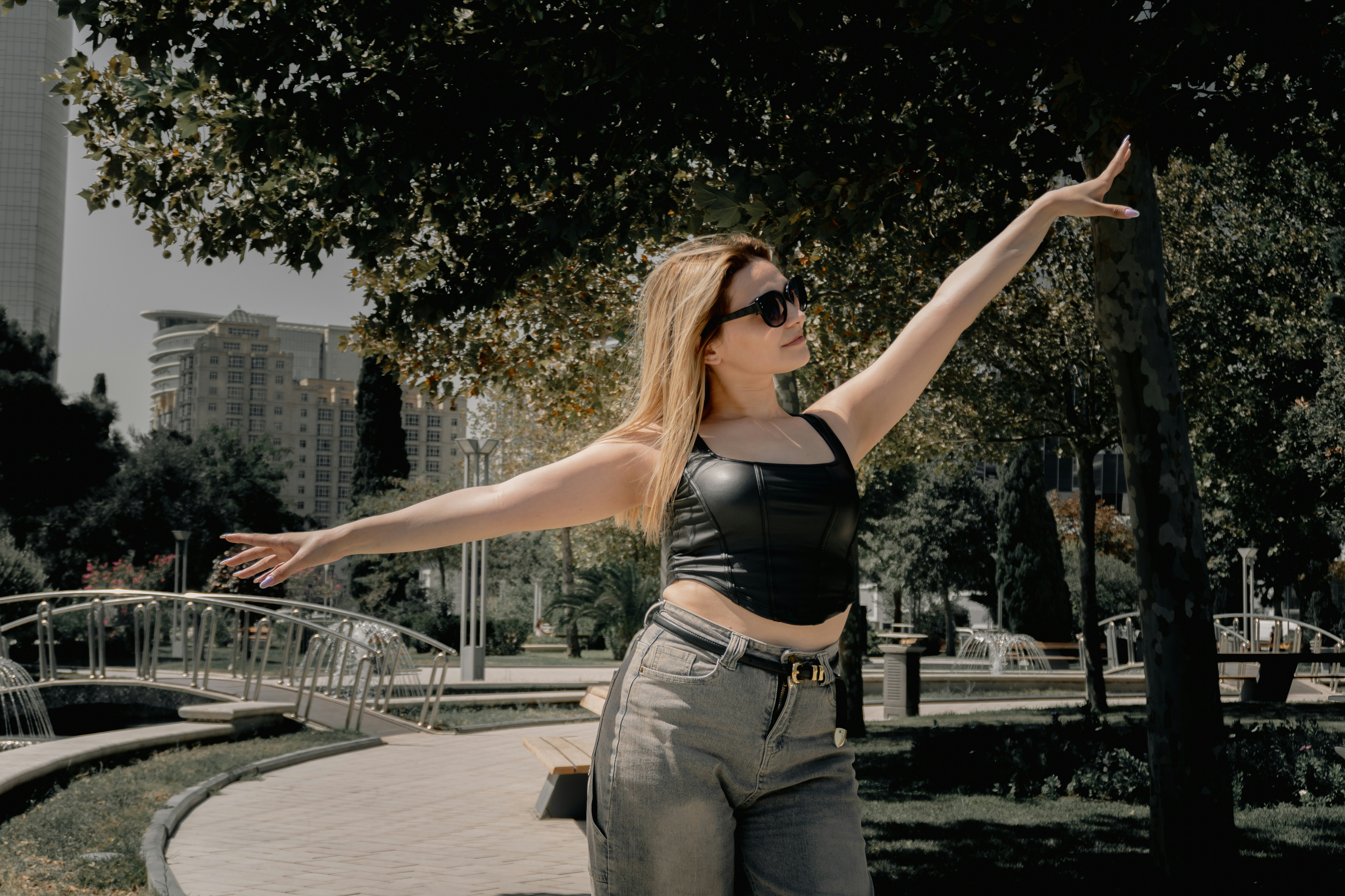 Blonde woman in sunglasses posing outdoors with arms raised