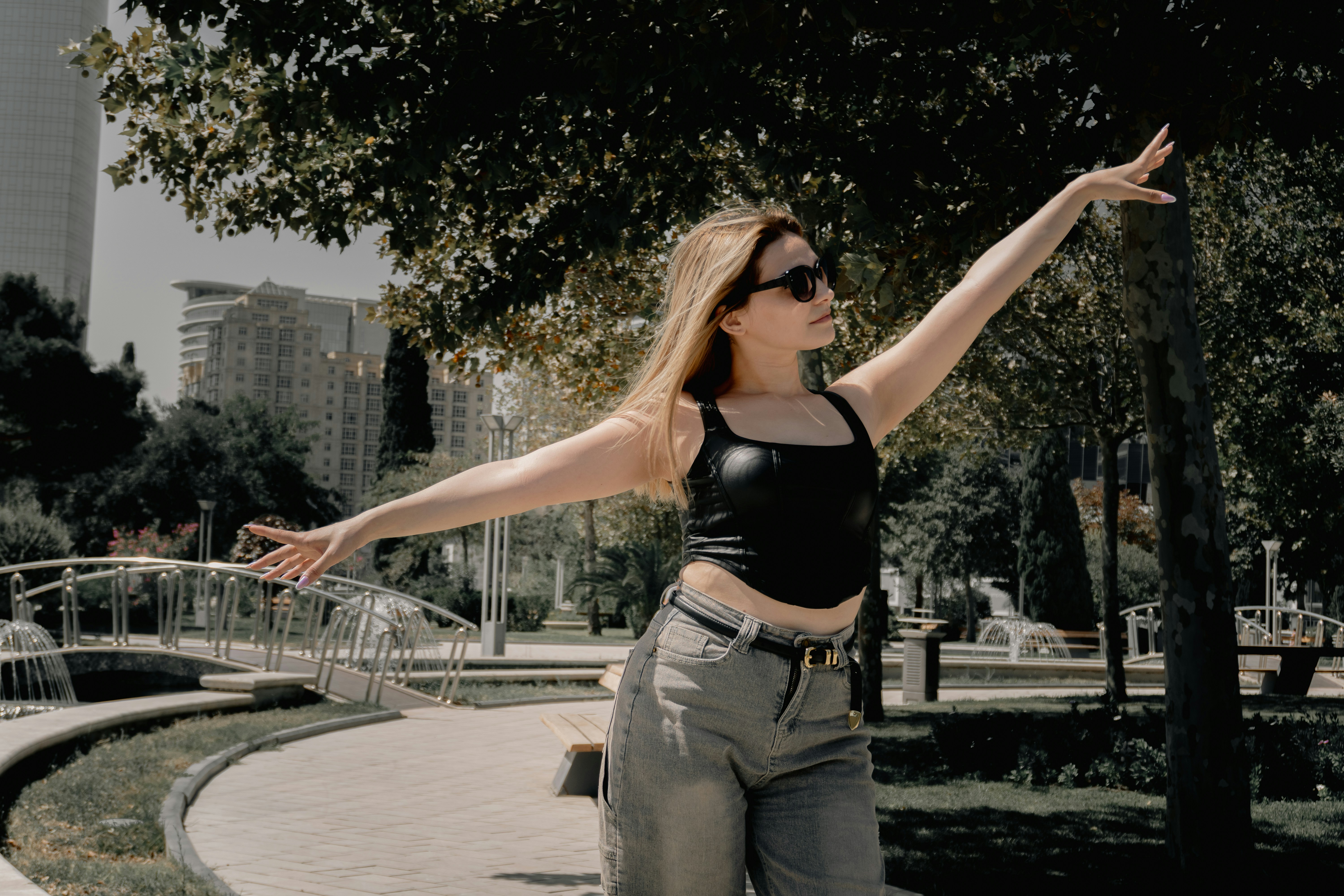 Young woman with outstretched arms posing in a sunny park.