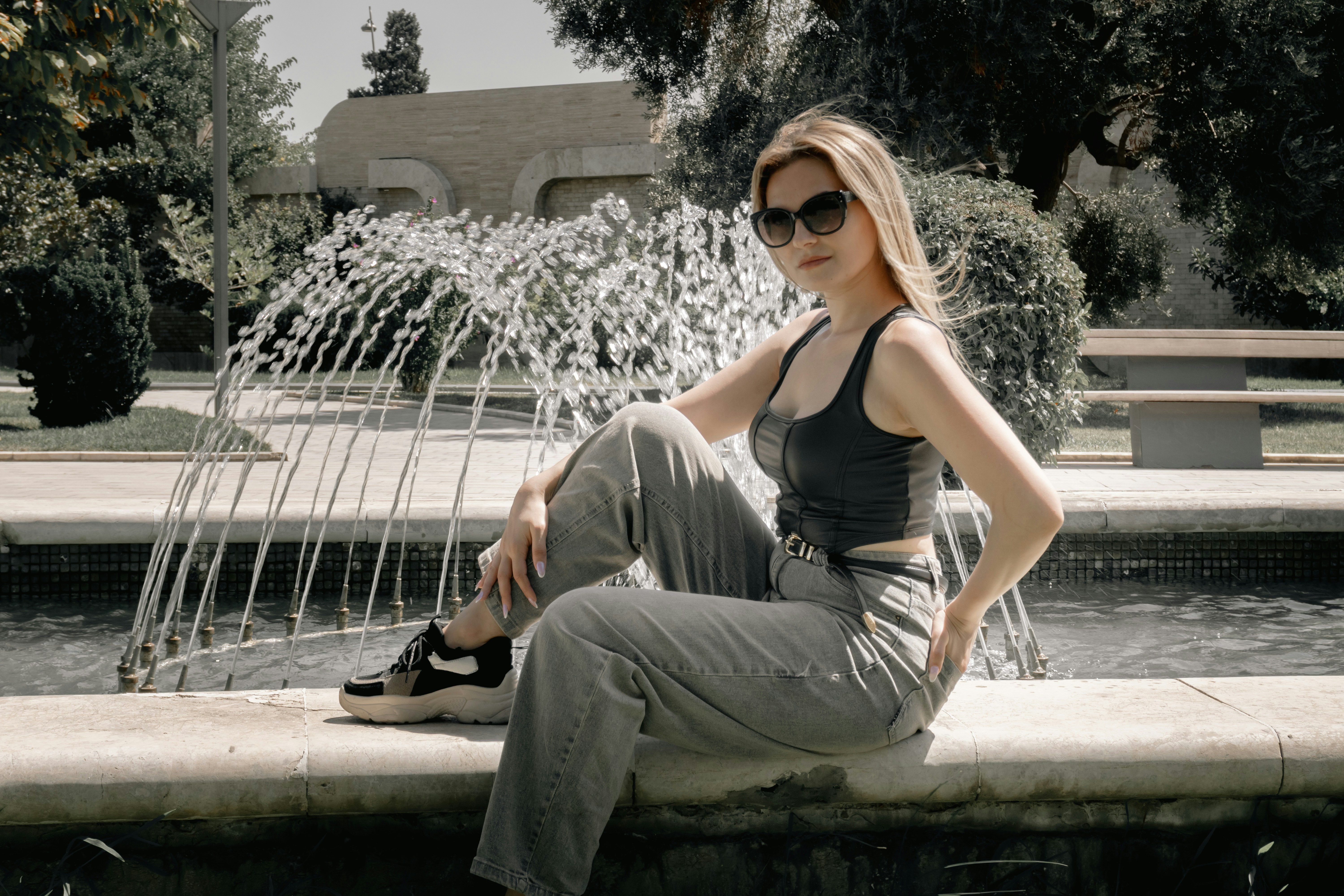 A young woman sits by a fountain in a park.