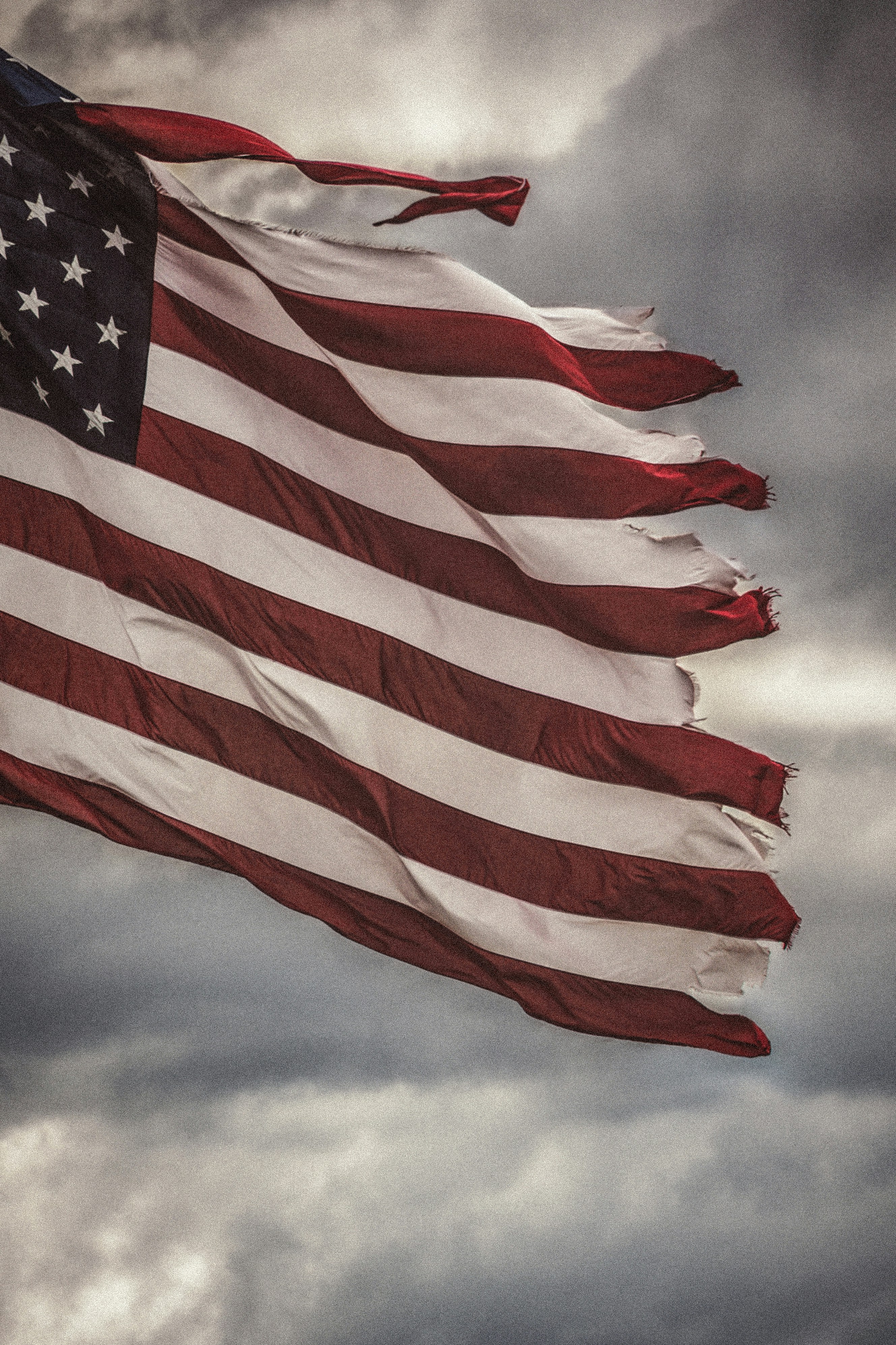 Tattered american flag against dark, stormy clouds