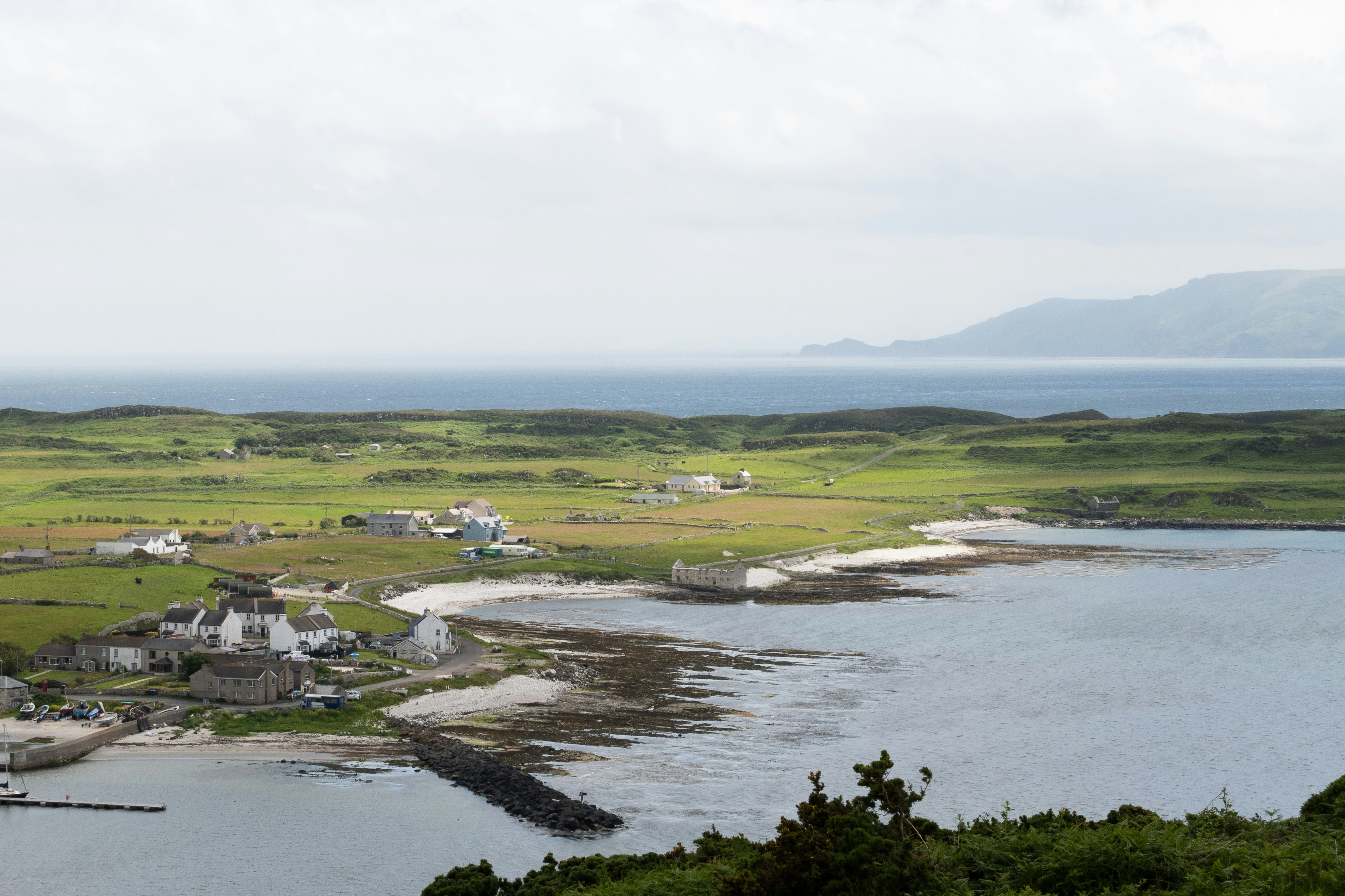 Village by the sea with green fields and distant mountains