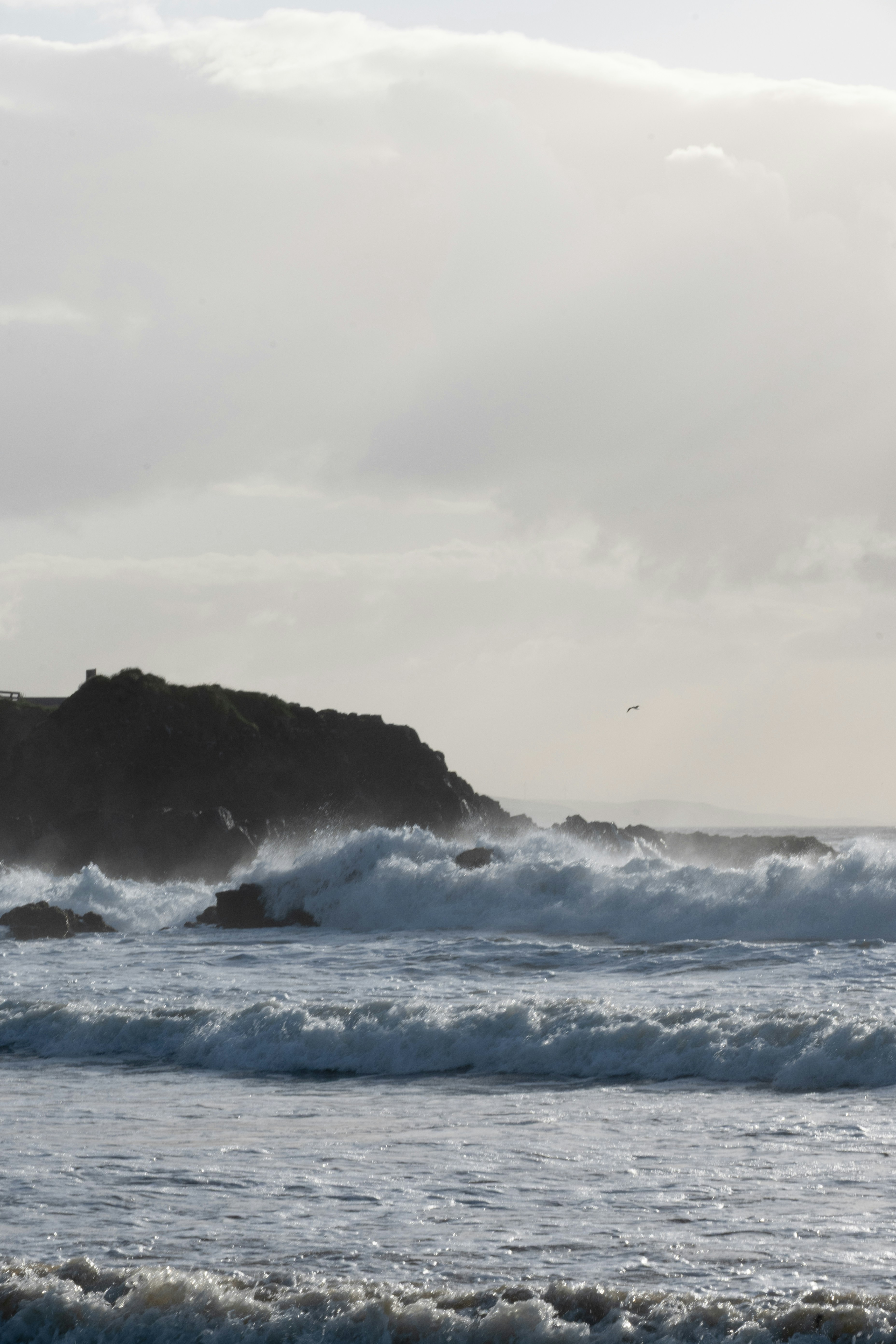 Crashing waves against a dark, rocky coast under cloudy sky
