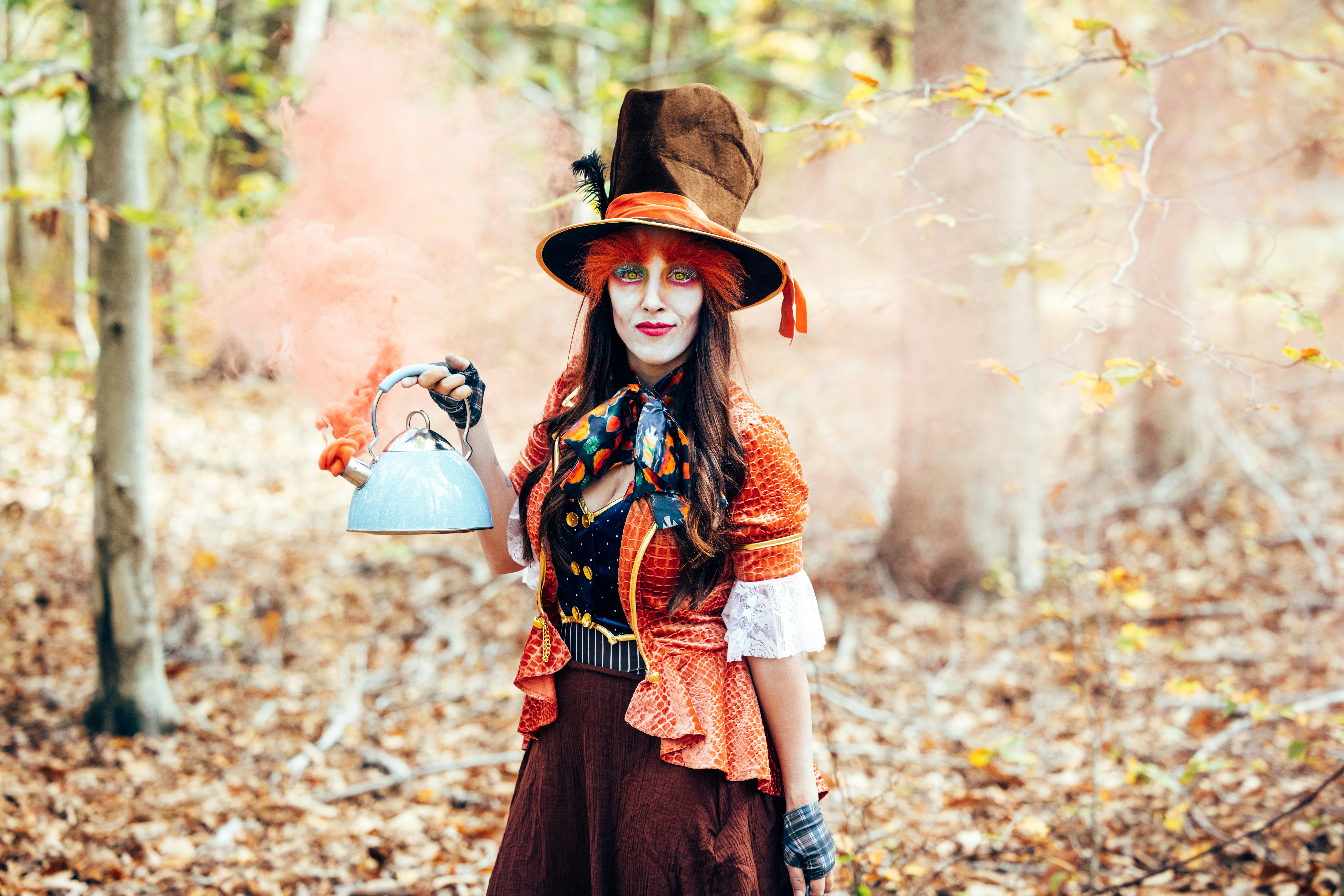 Frau im Mad Hatter-Kostüm hält eine Teekanne mit orangefarbenem Rauch