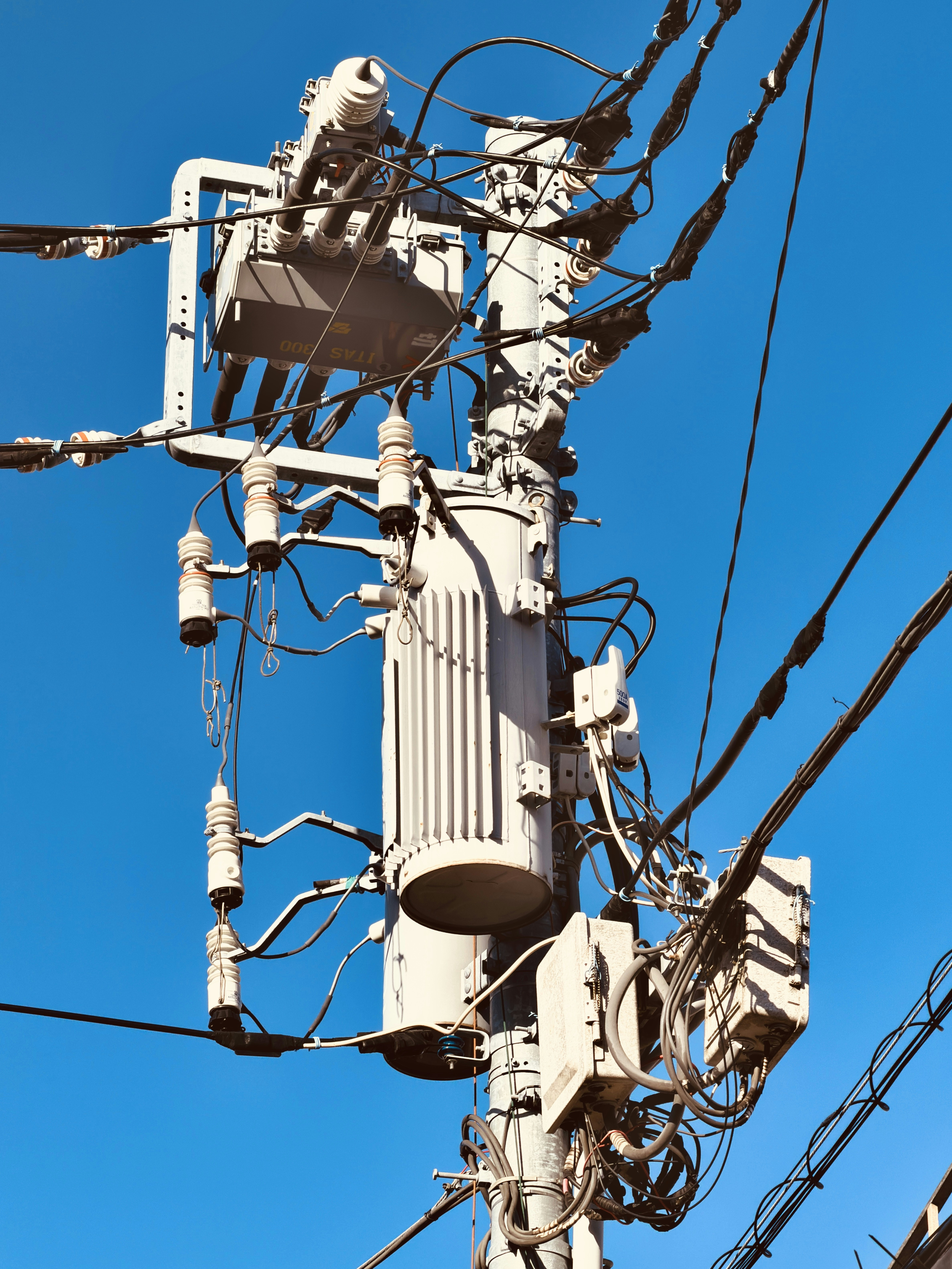 Poli elettrico con fili e trasformatori contro il cielo azzurro.
