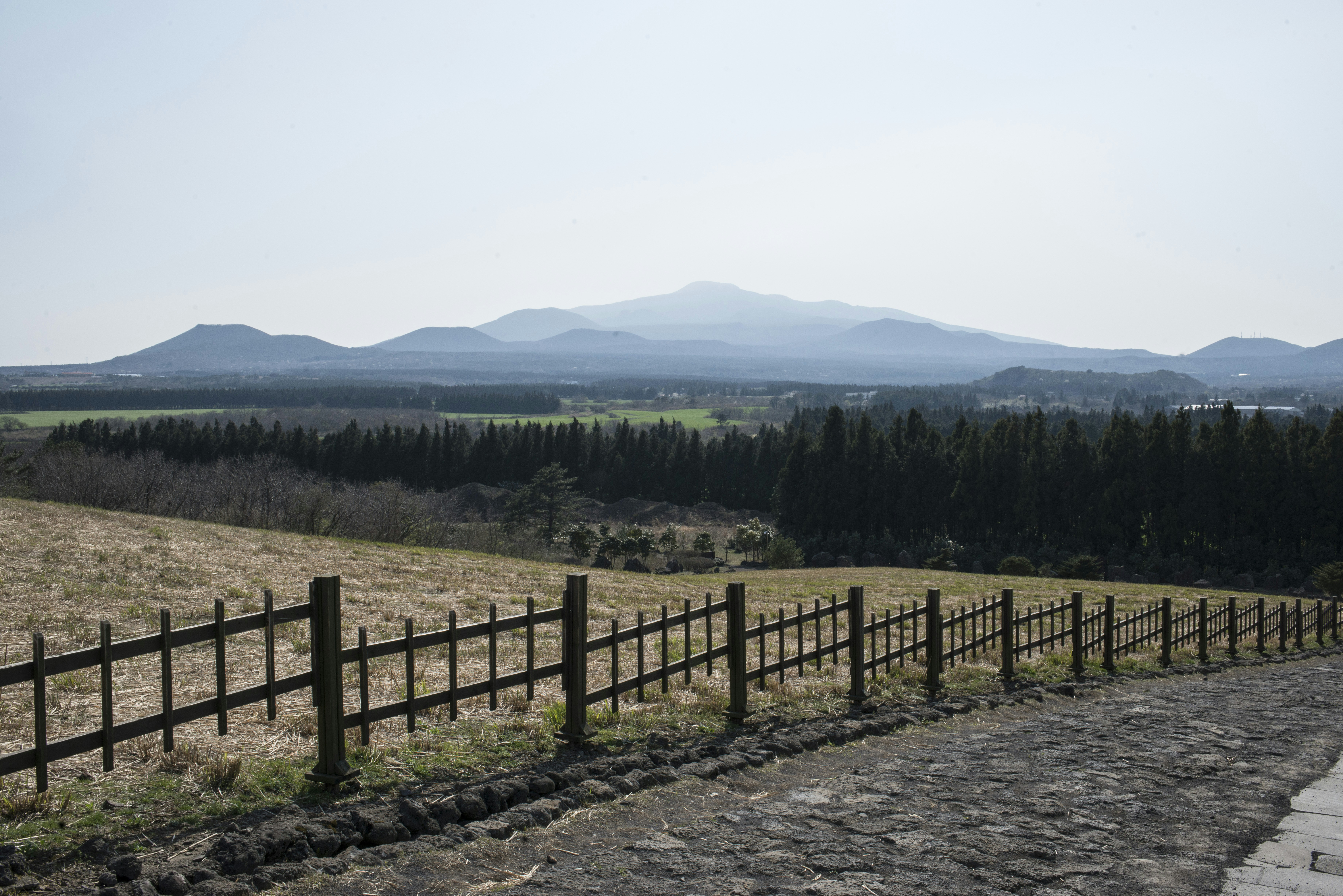 A wooden fence separates fields from a distant mountain range