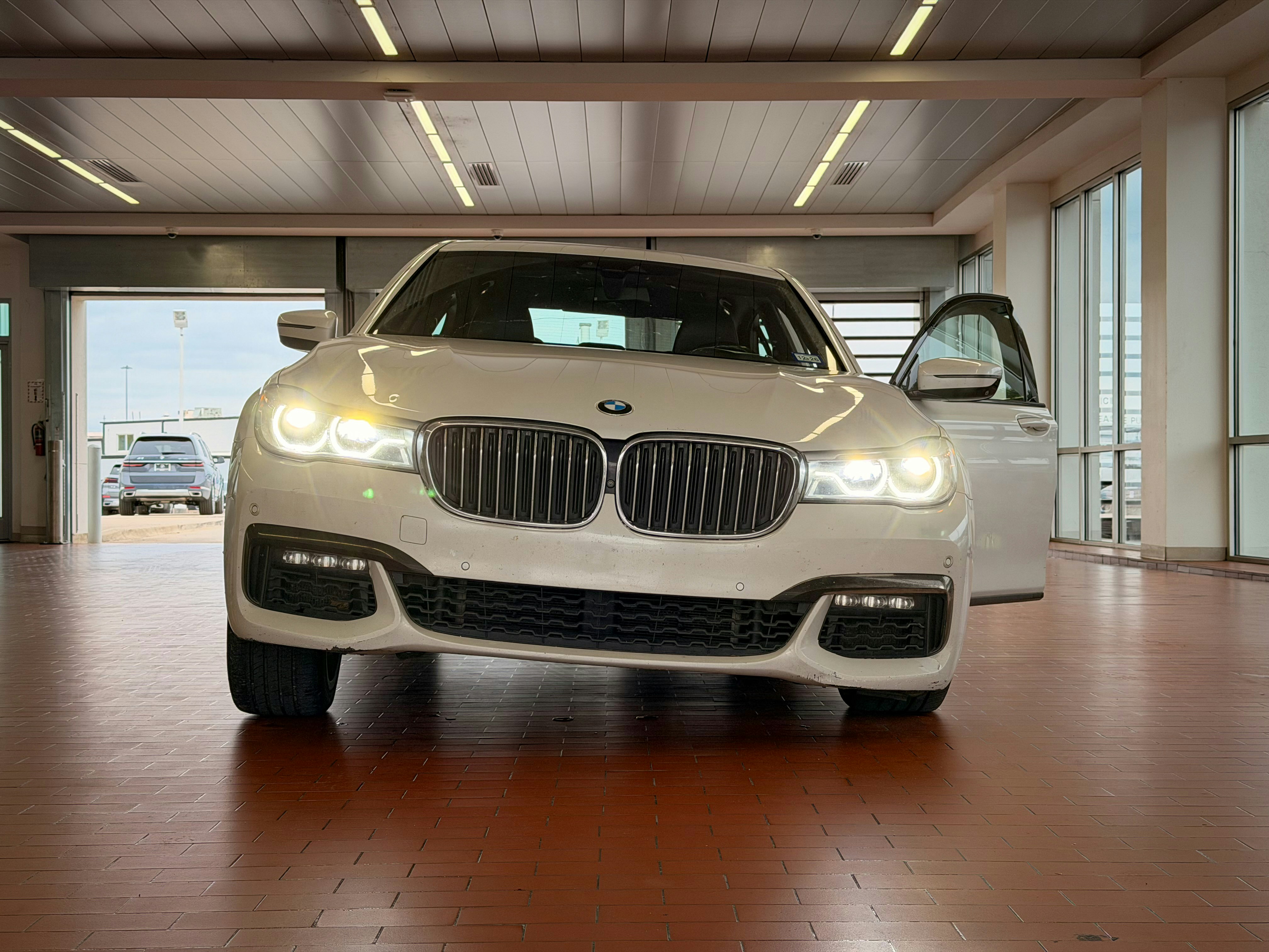 White BMW sedan with bright headlights and open driver's door.