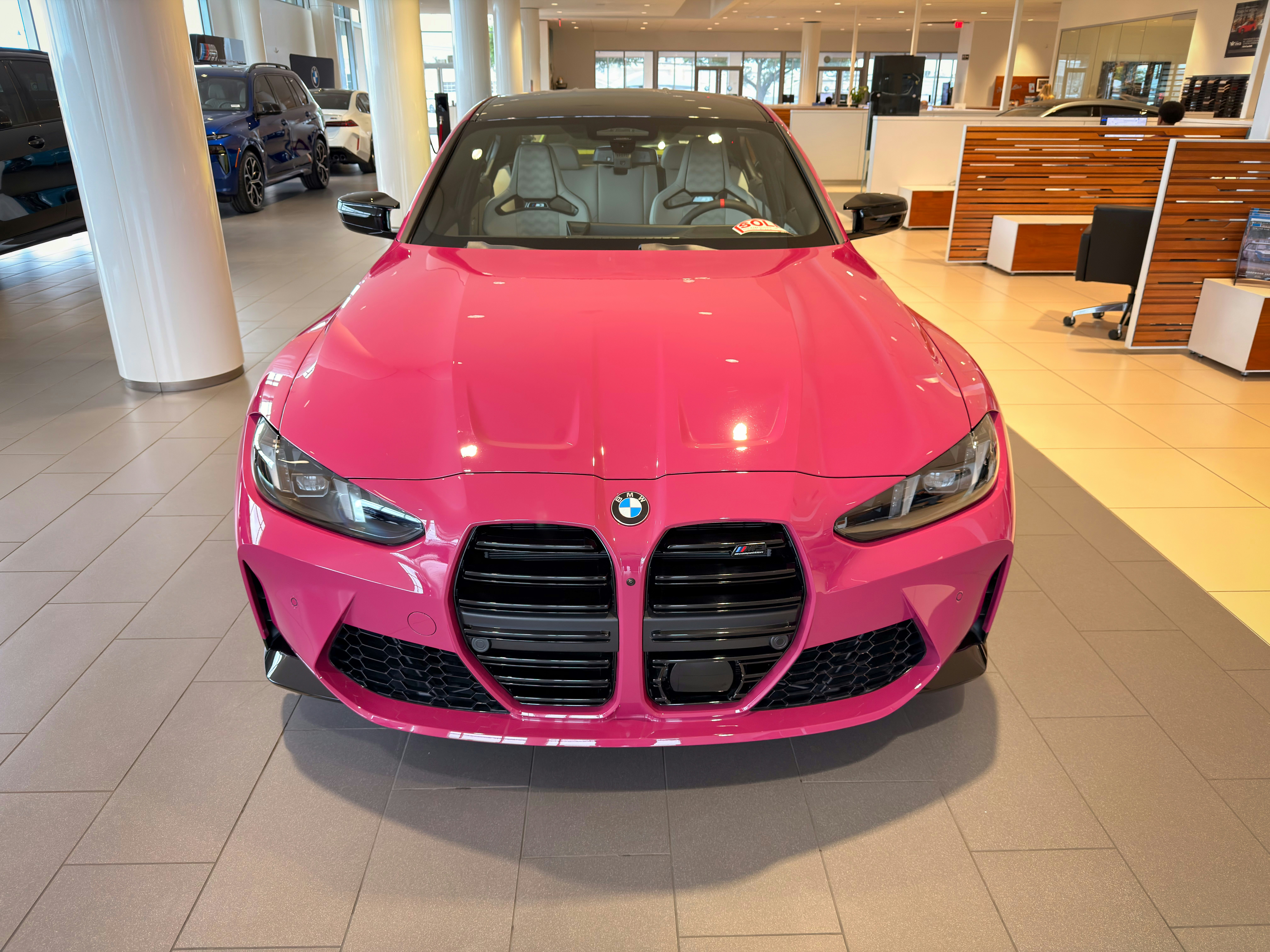 Ein leuchtend pinkes BMW-Auto, das in einem modernen Ausstellungsraum geparkt ist.