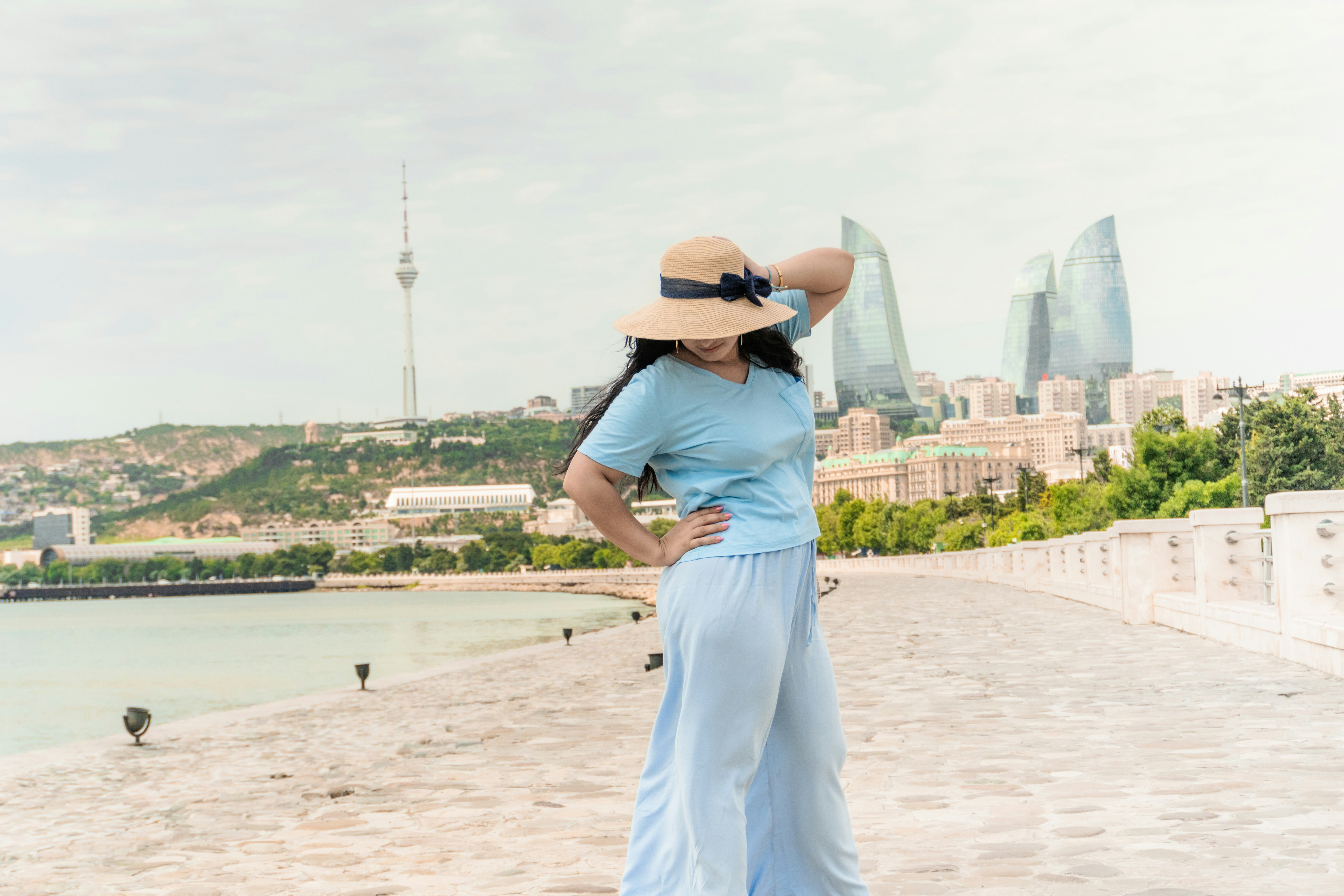 Woman in hat on pier with city skyline and water.
