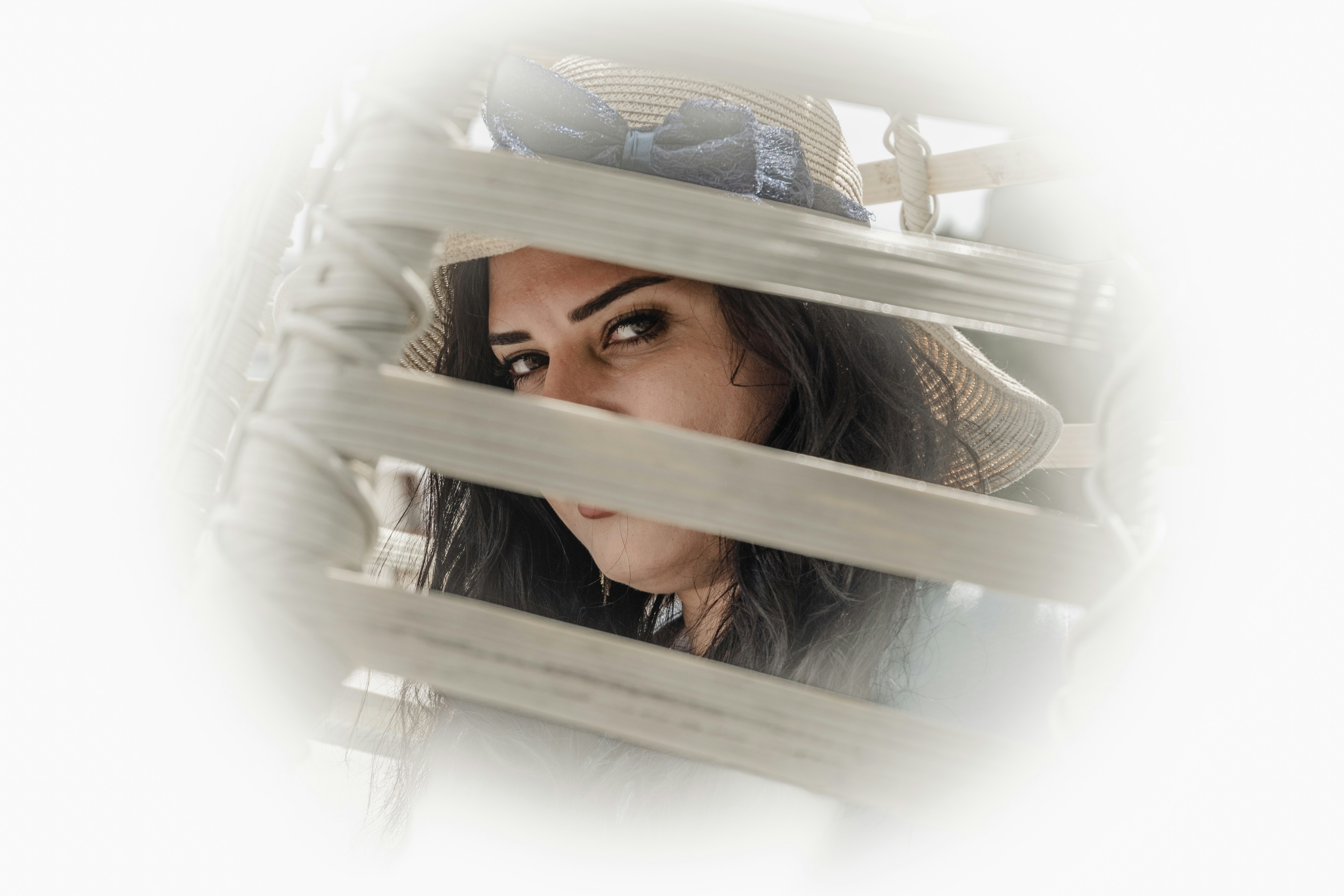 Geheimnisvolle Frau, die durch weiße horizontale Jalousien lugt.