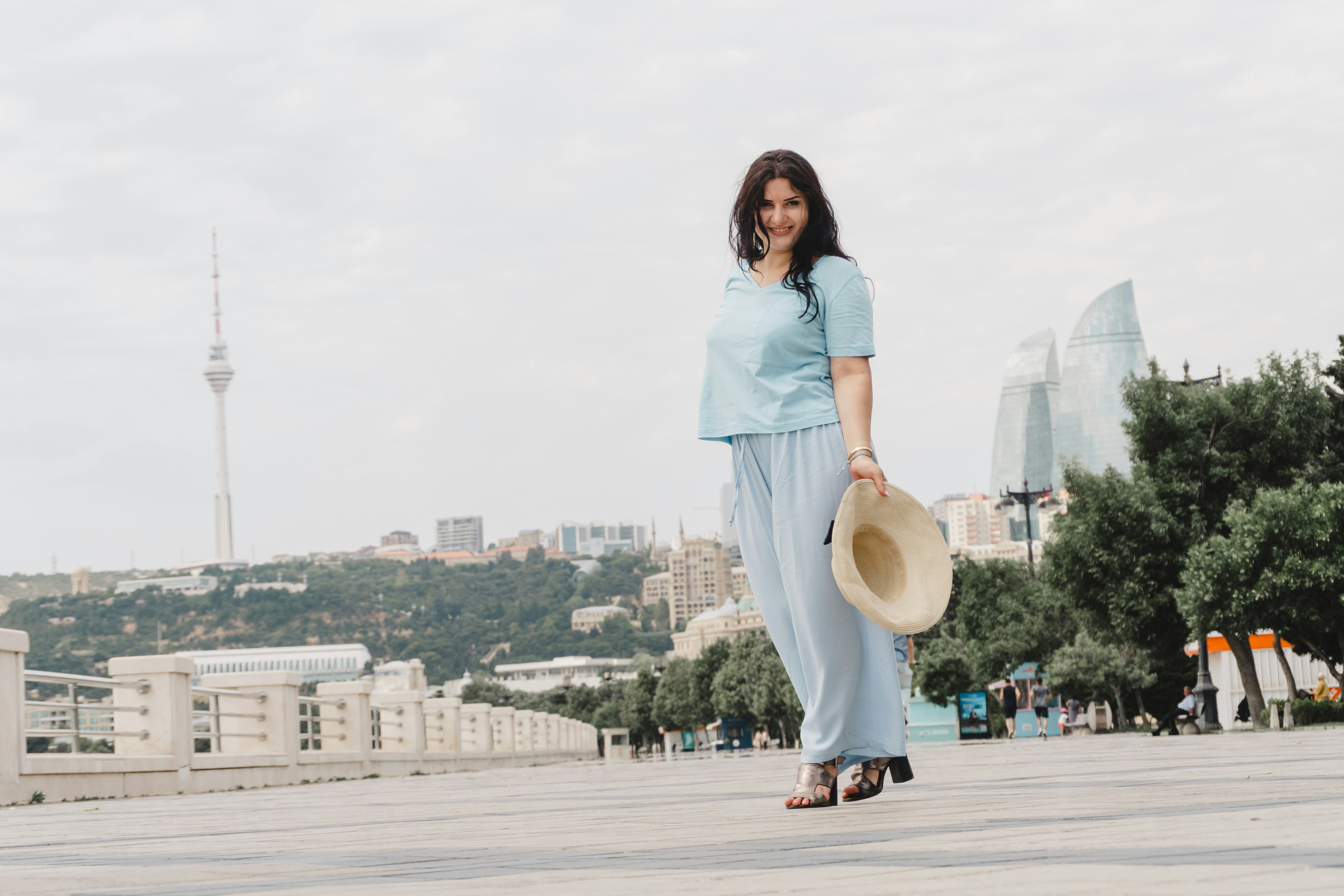 Smiling woman holding a hat with a city skyline background.