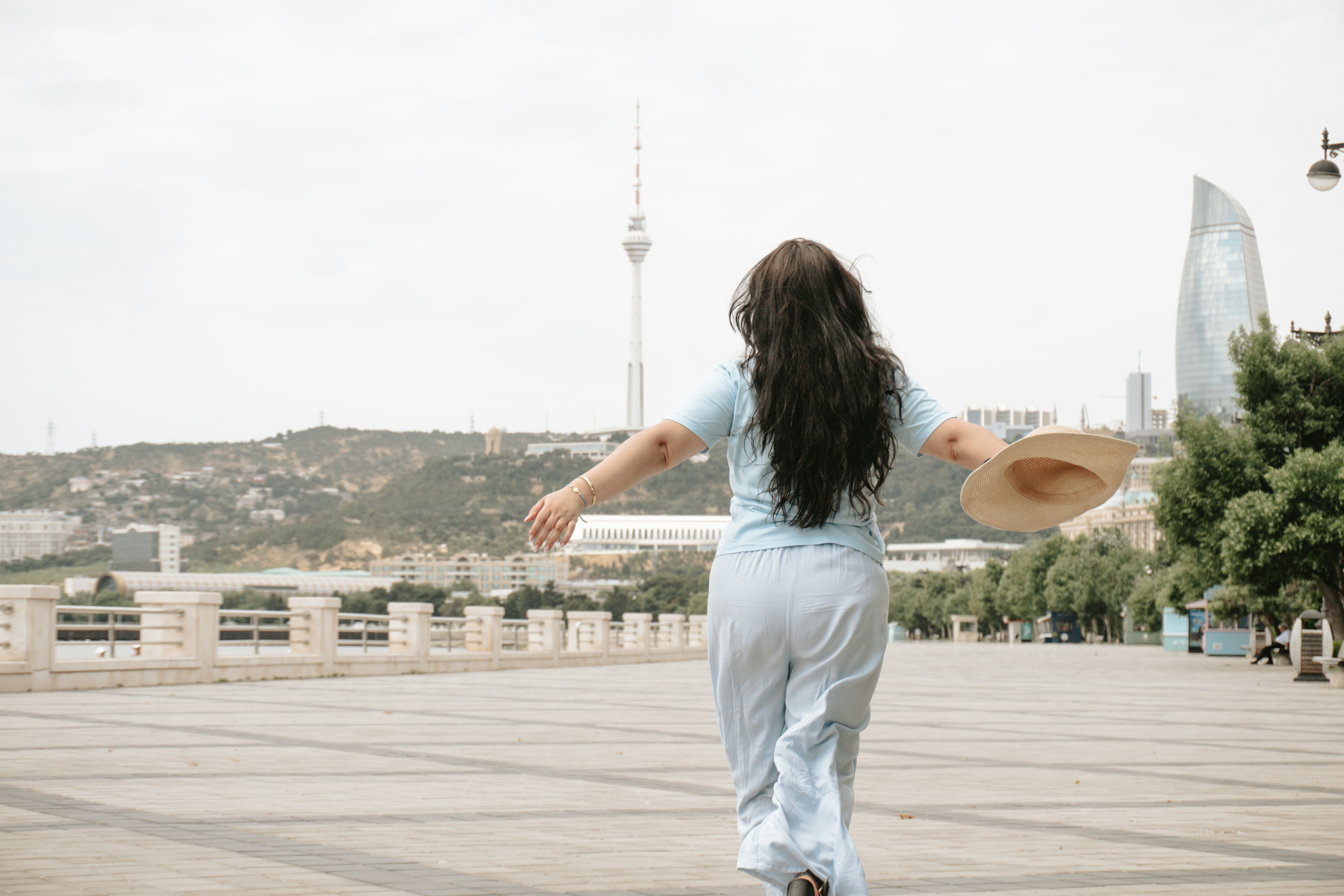A woman walking away with a hat towards a cityscape