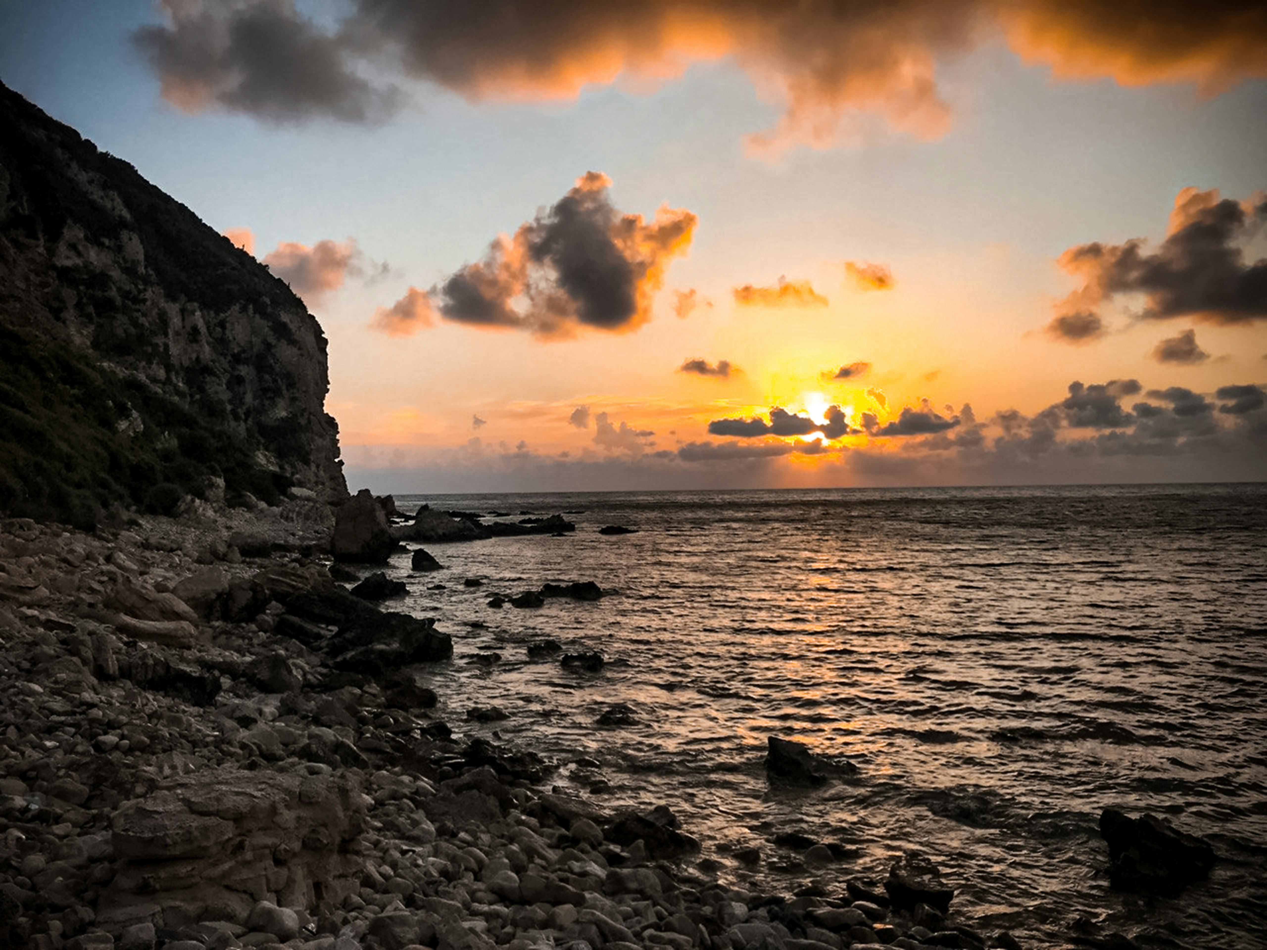Sunset over a rocky ocean with a cliff