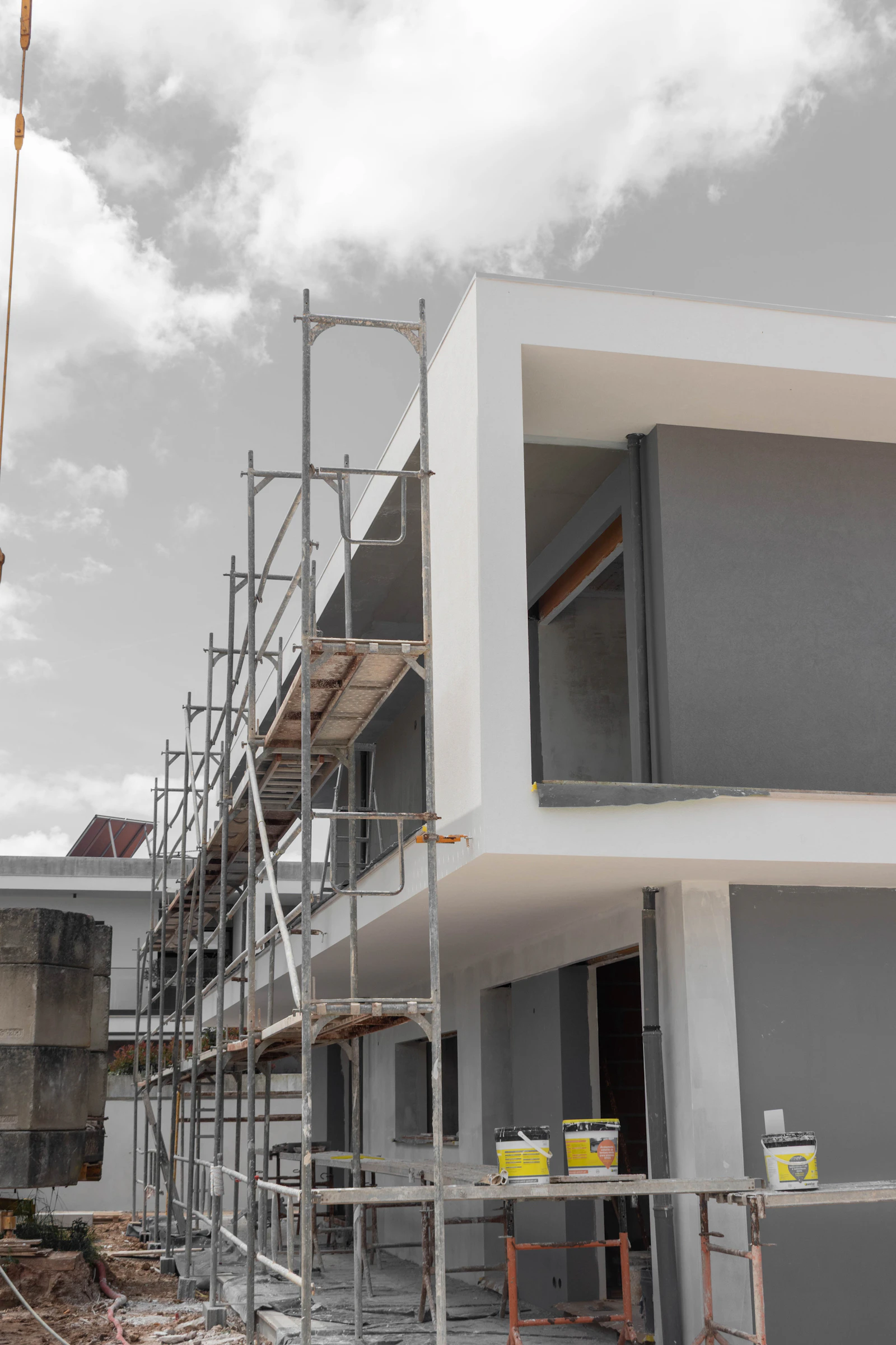 Eingerüsteter heller Neubau mit Flachdachanbau und Baumaterial im Vordergrund