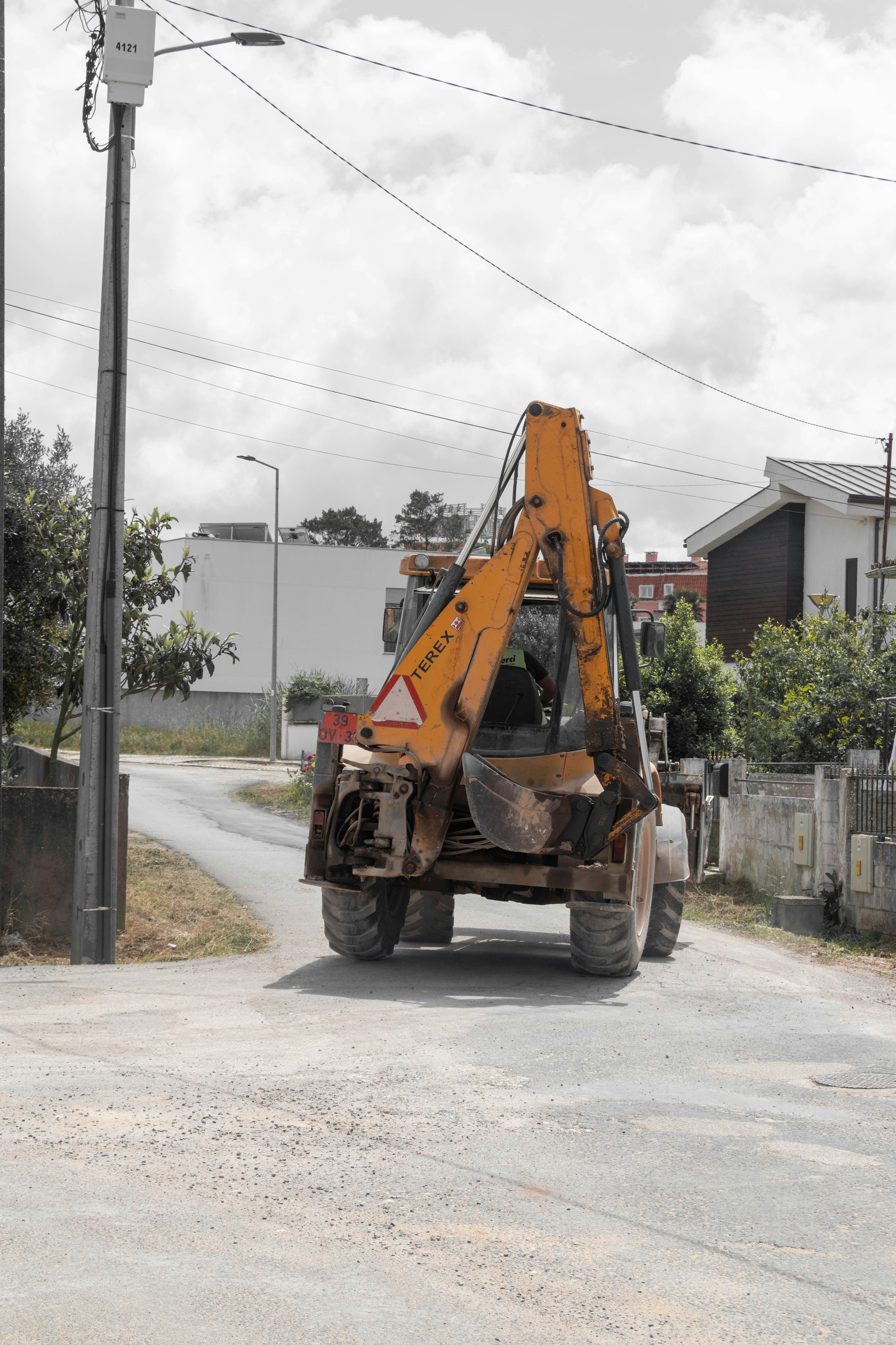 An orange backhoe loader drives on a dirt road