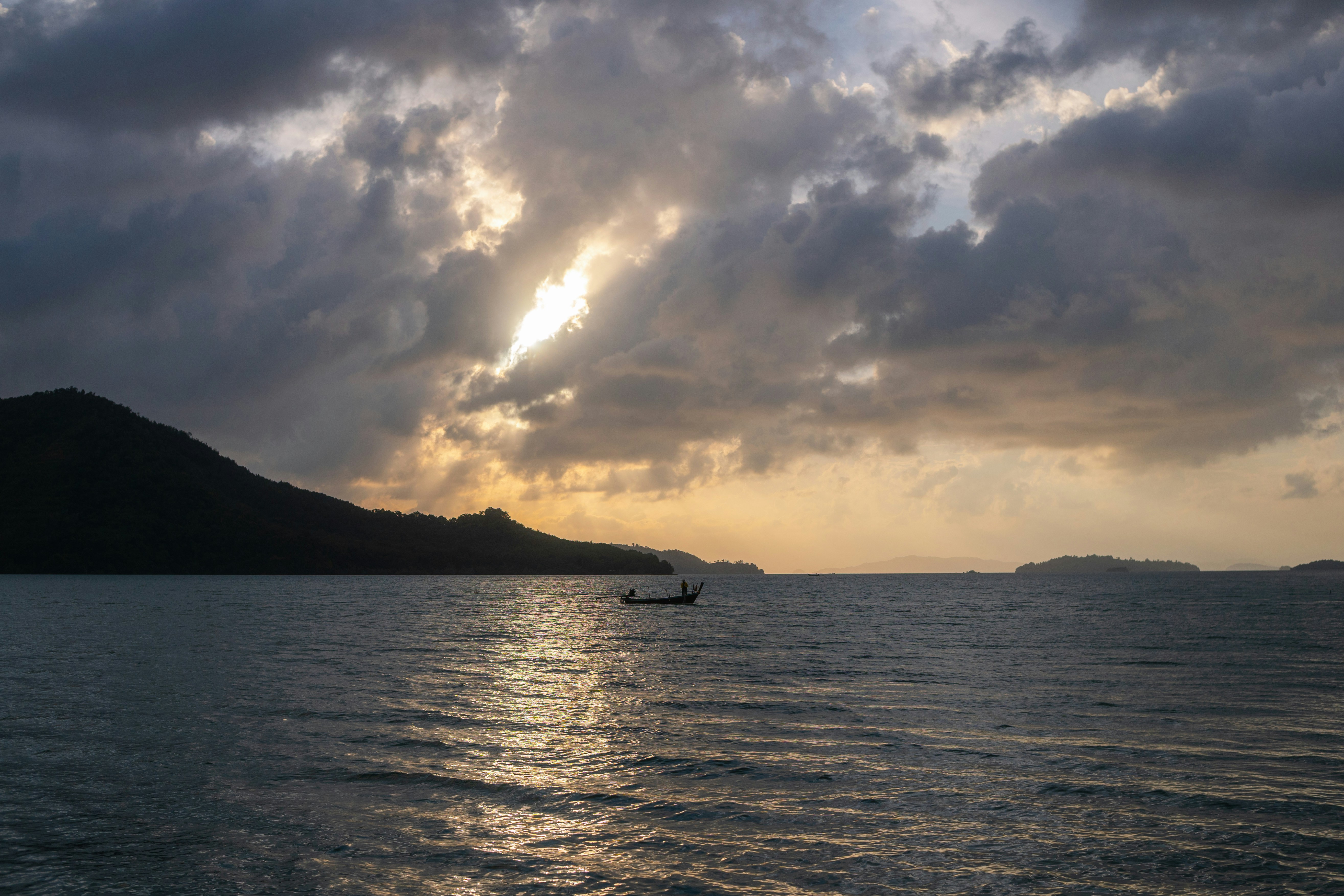 Un coucher de soleil spectaculaire sur l’océan avec un petit bateau et des montagnes.