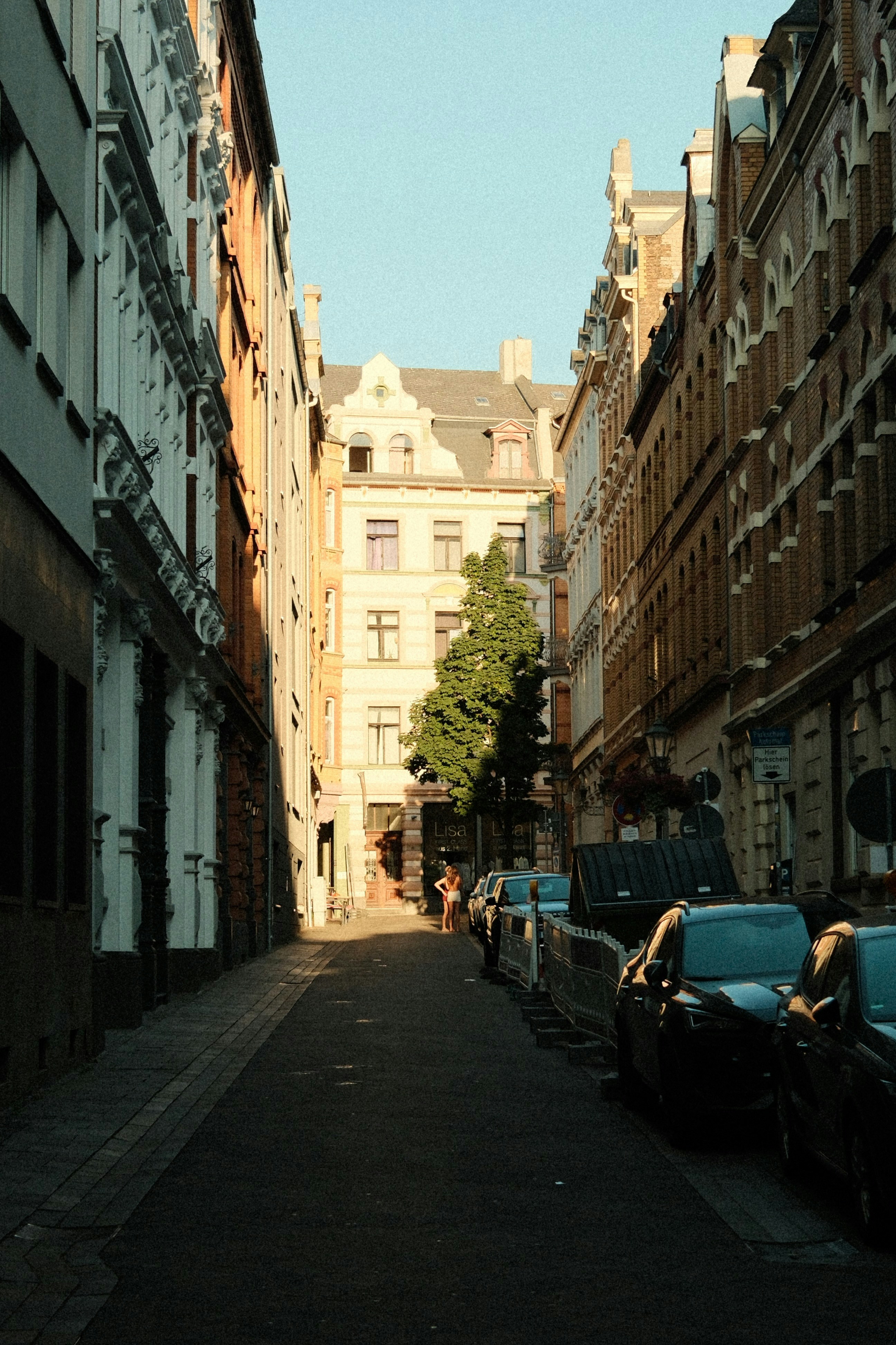 A narrow european street with tall buildings and parked cars