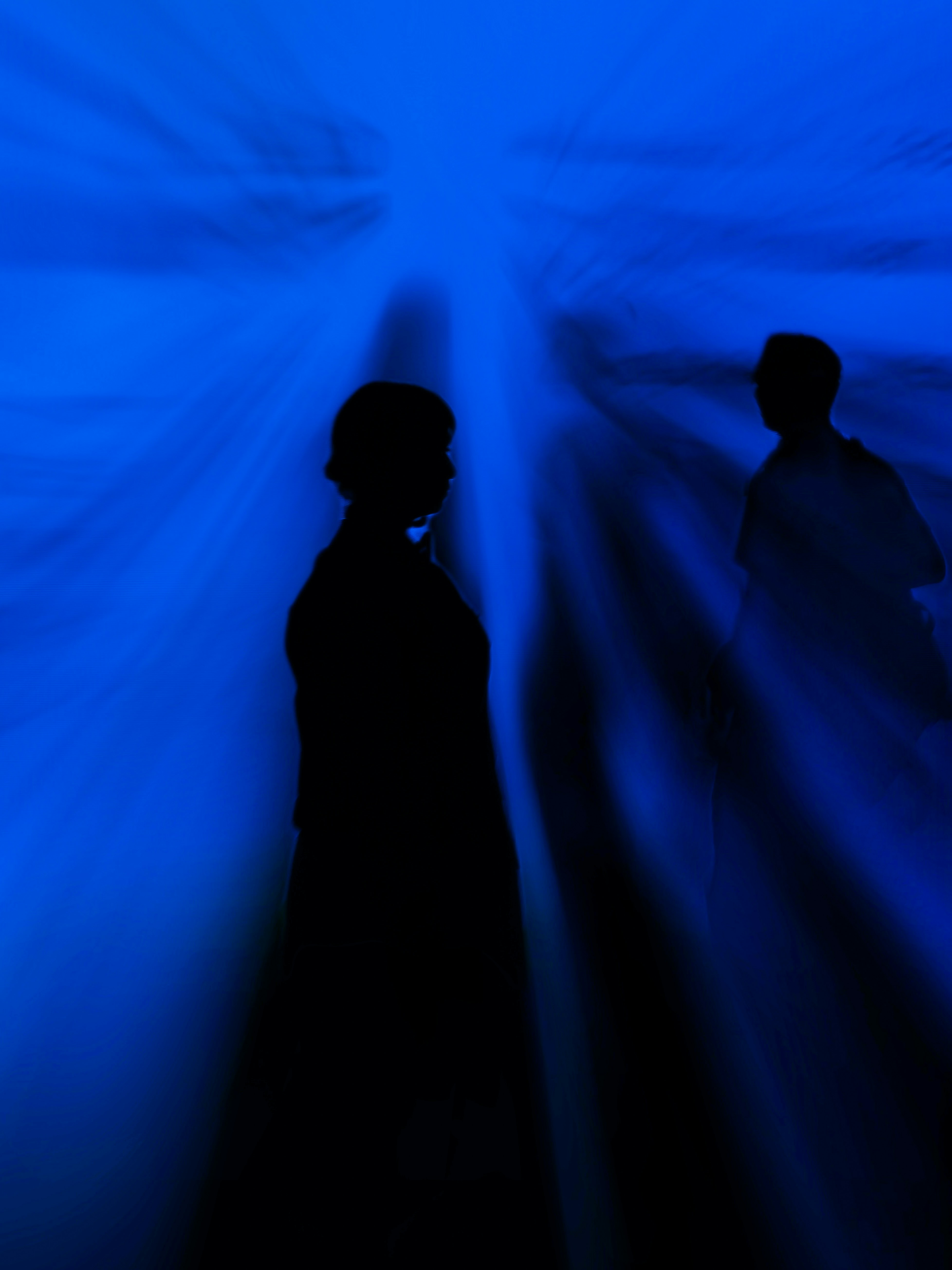 Two silhouettes against a vibrant blue background with light rays