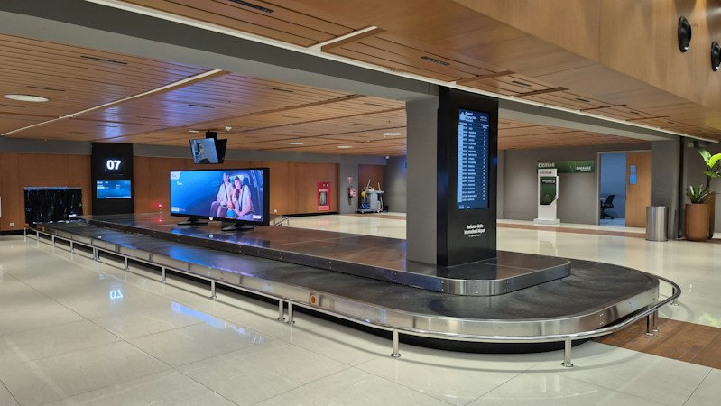 A modern airport baggage claim carousel with digital screens overhead, the kind of upgraded claim area travelers can expect at Harry Reid