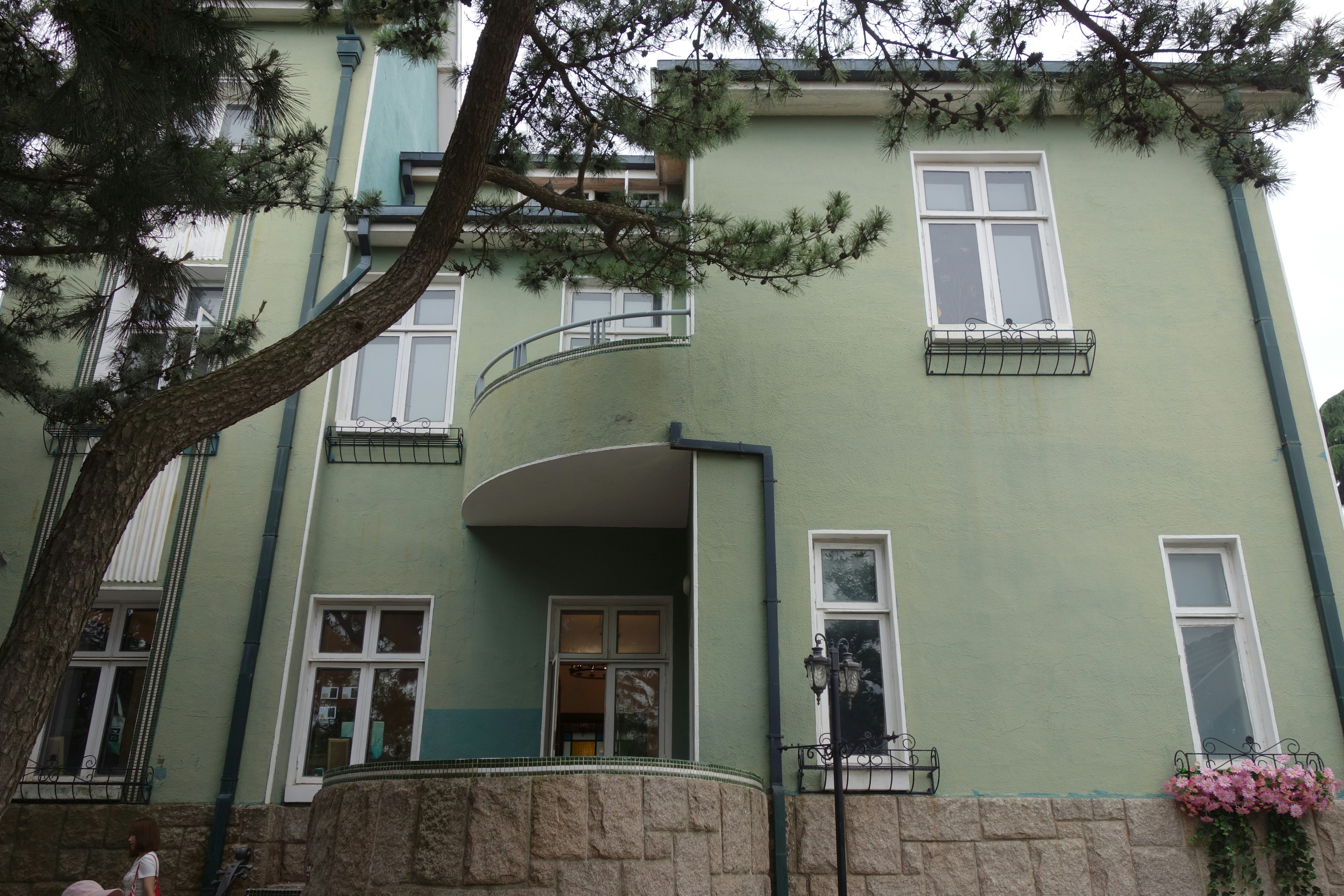 A light green building with white windows and a tree.