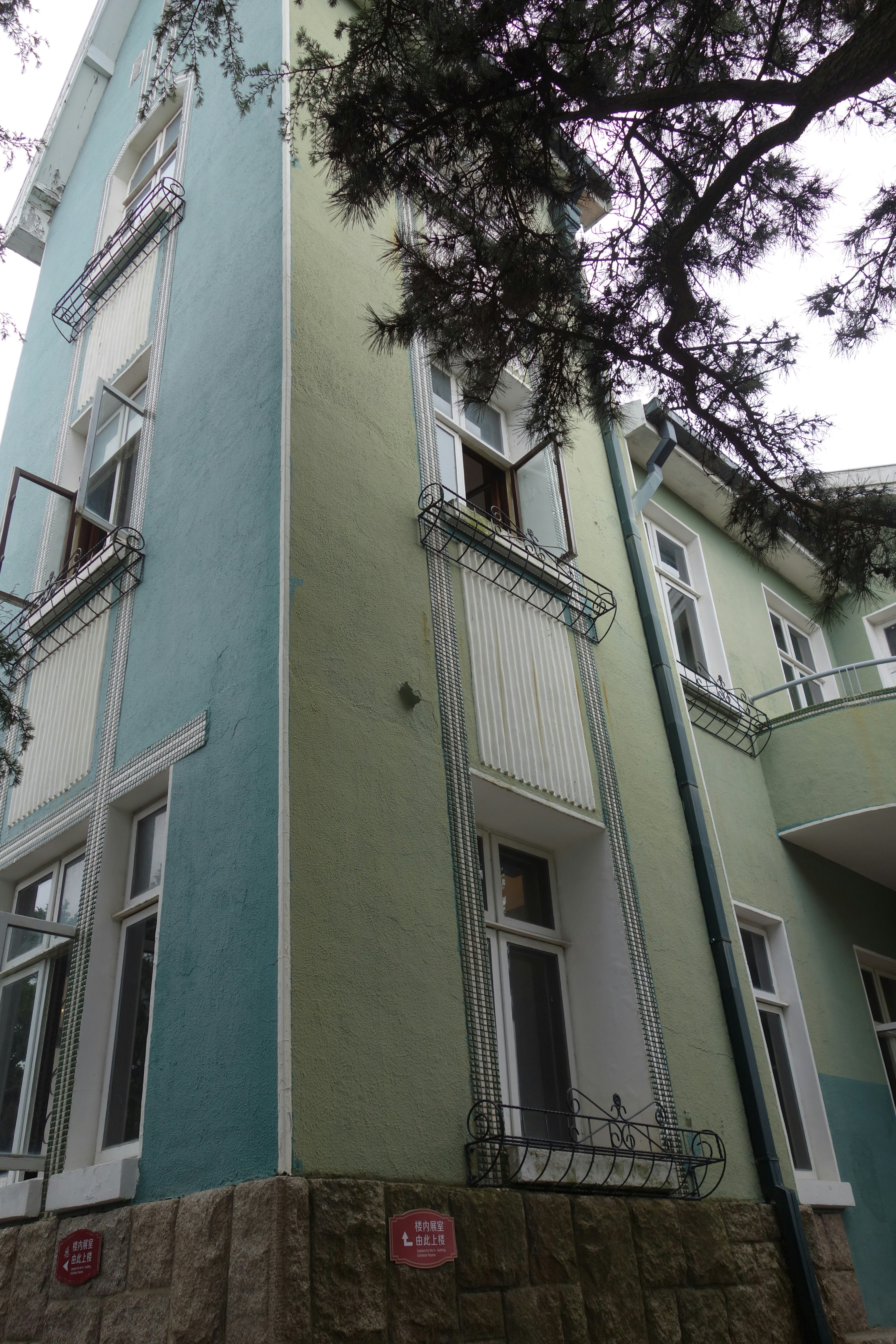 Light blue and green building with many windows and tree.