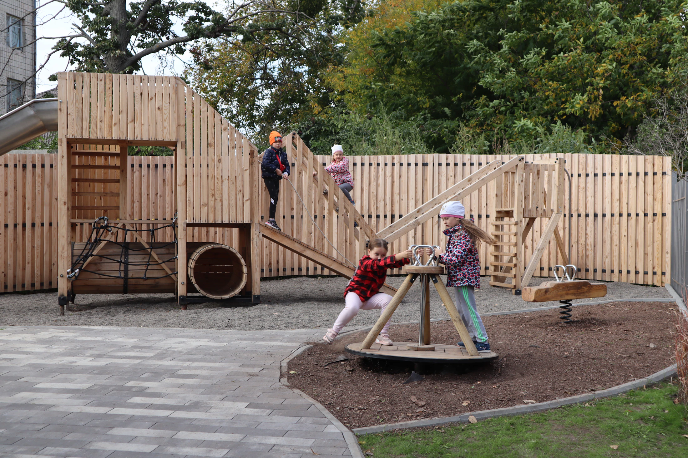 Children playing on a wooden playground in a leafy park