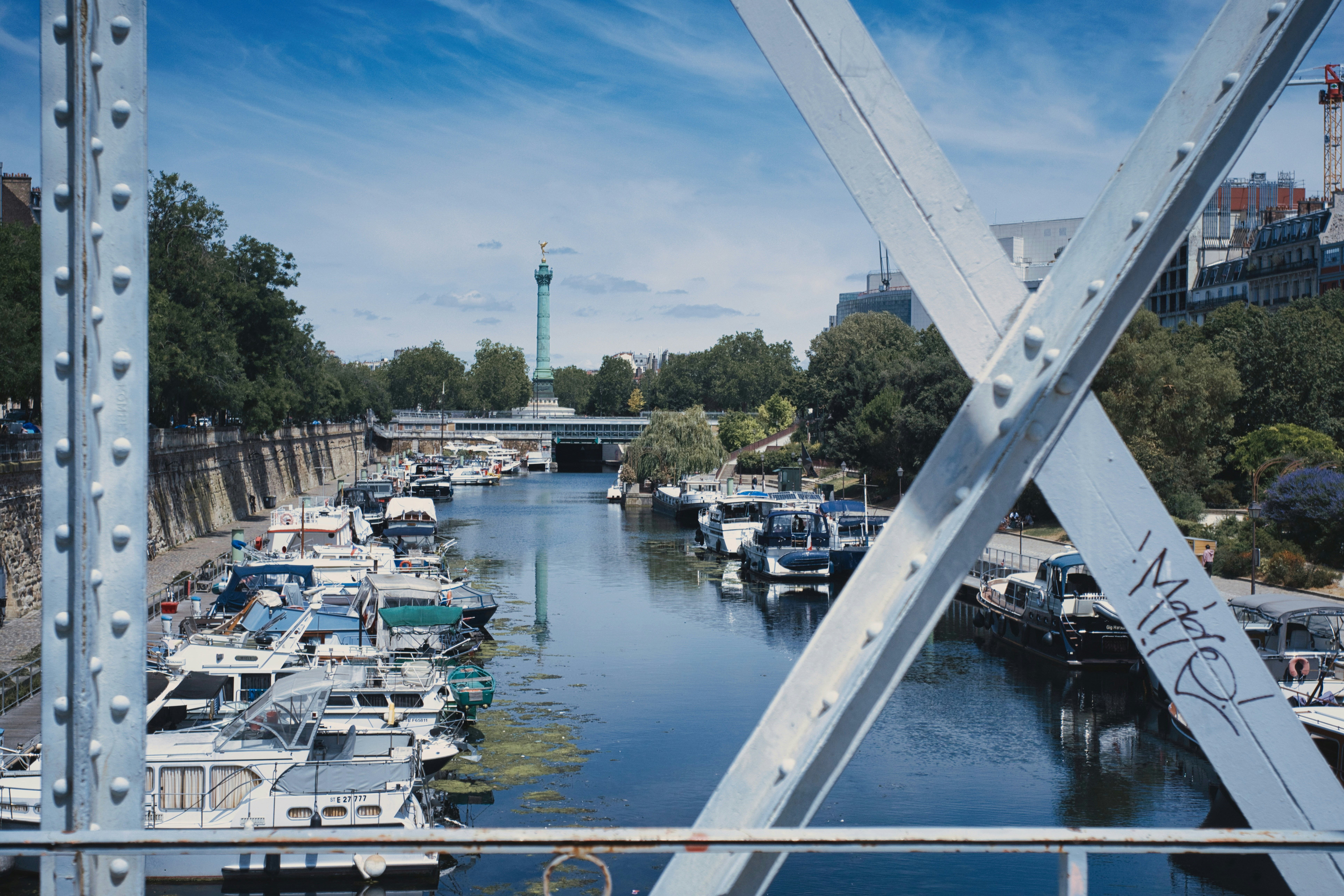 Canal lined with boats, framed by a metal bridge.