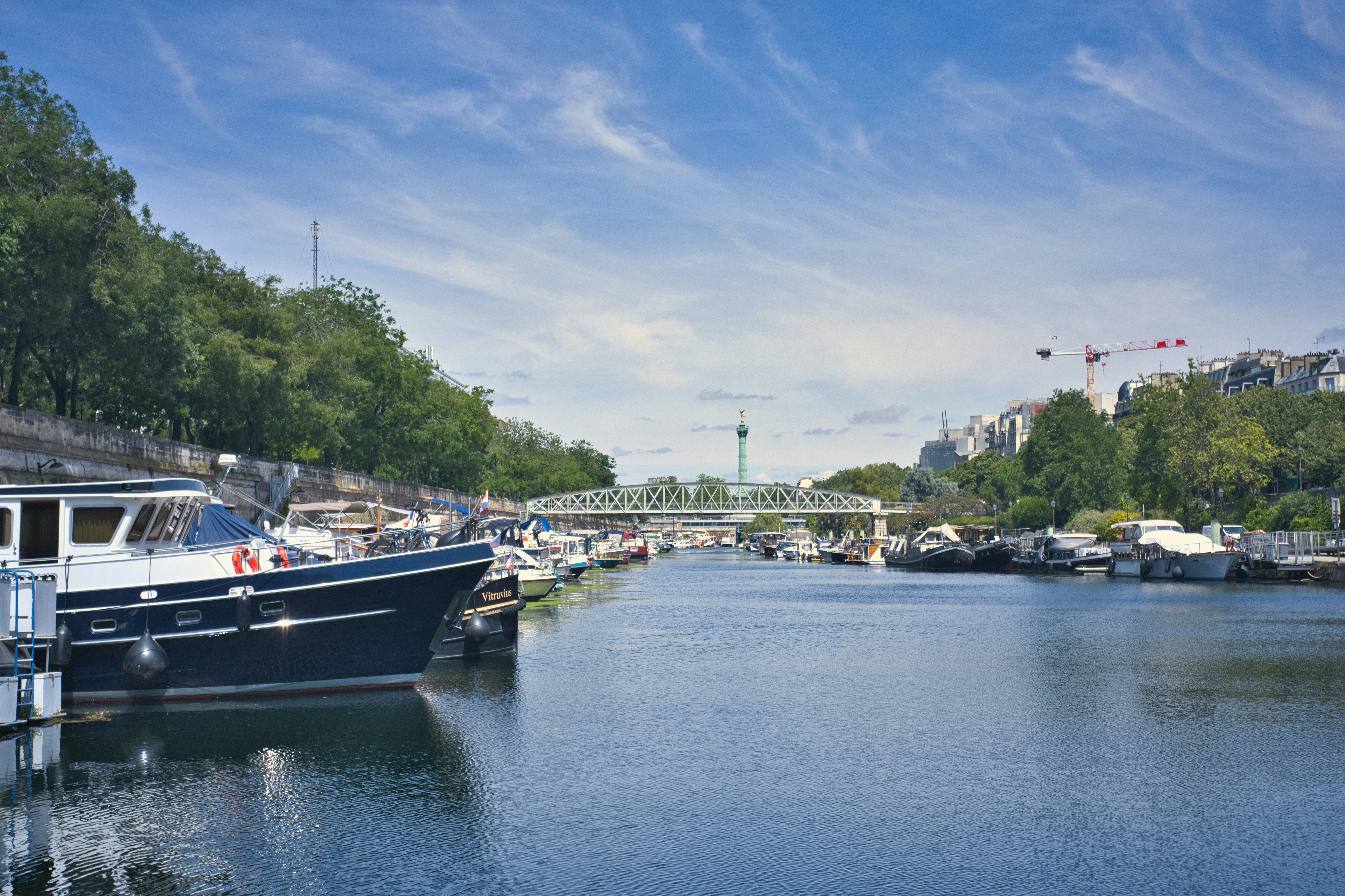 Boats docked in a canal with trees and a bridge.