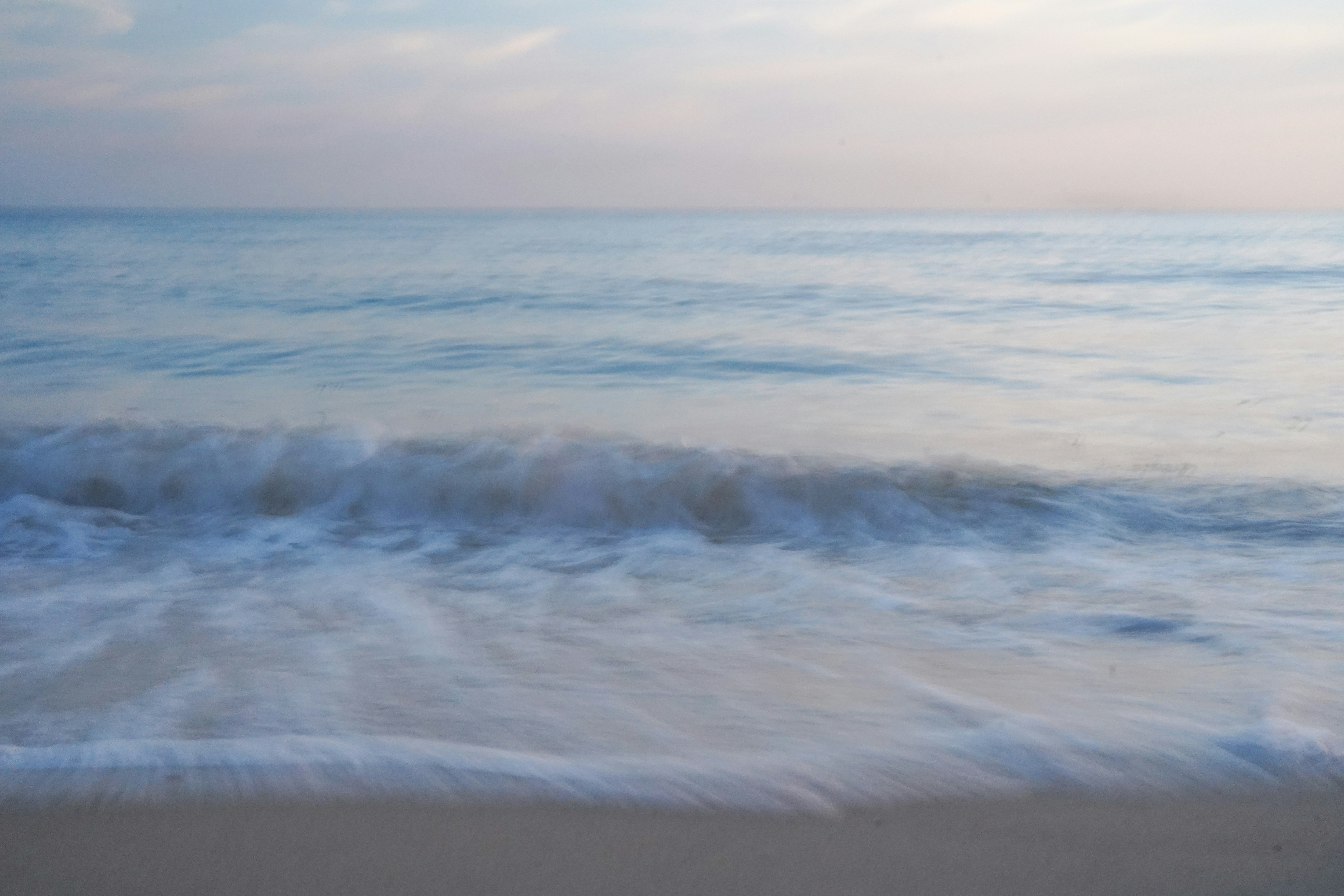 A soft ocean wave rising and cresting toward a quiet beach