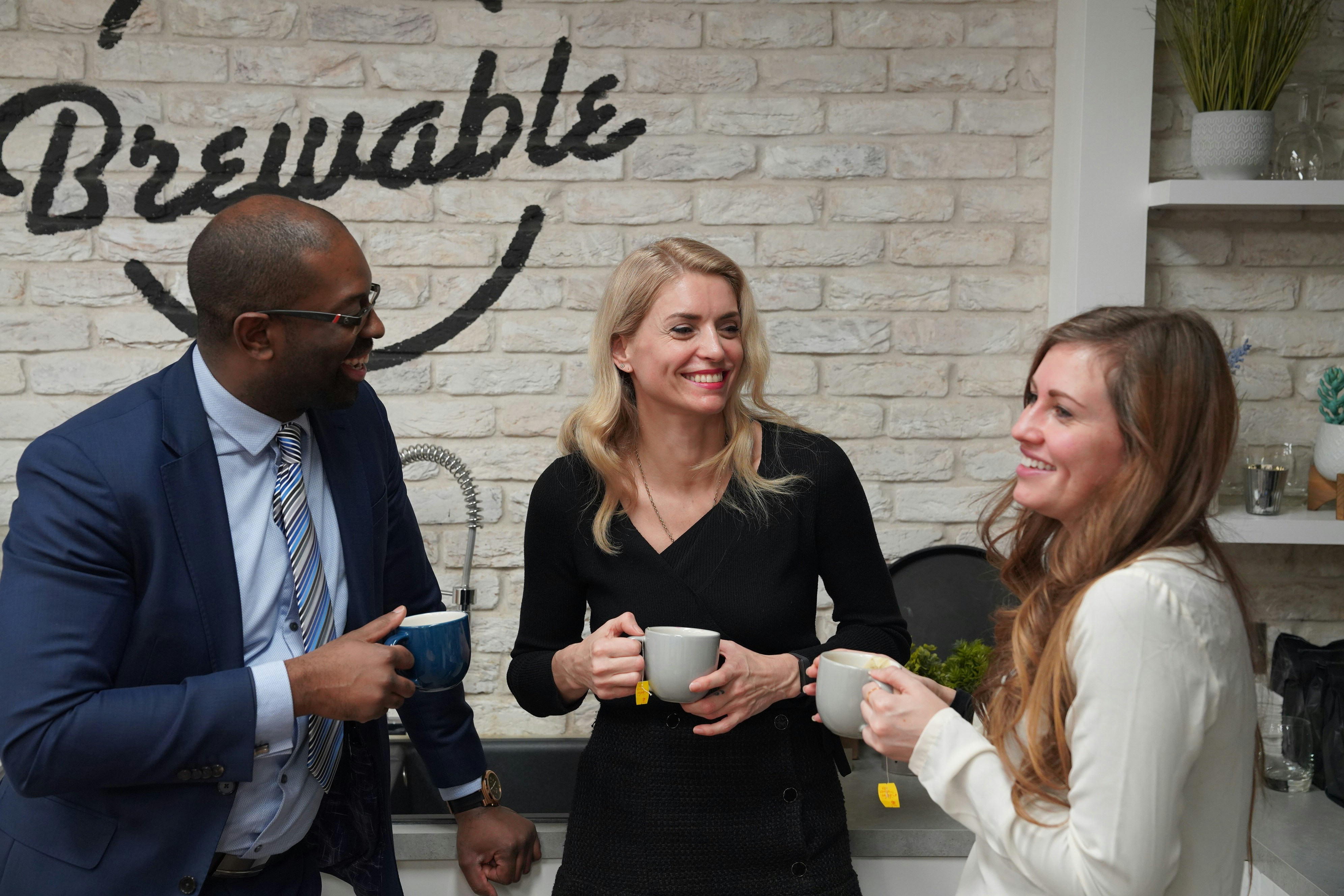 Three colleagues holding mugs in an office kitchen
