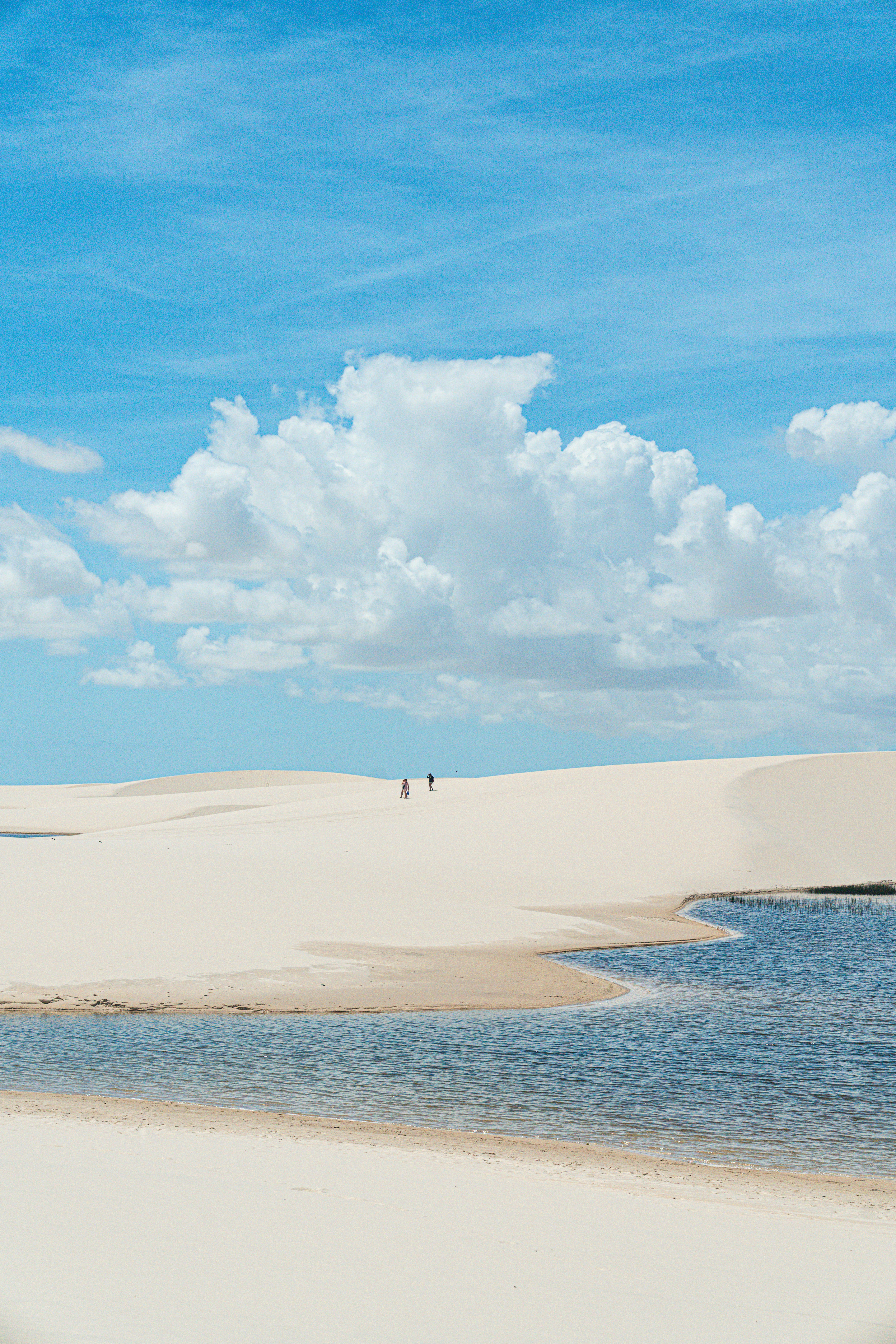 As pessoas caminham por vastas dunas de areia com uma lagoa azul.