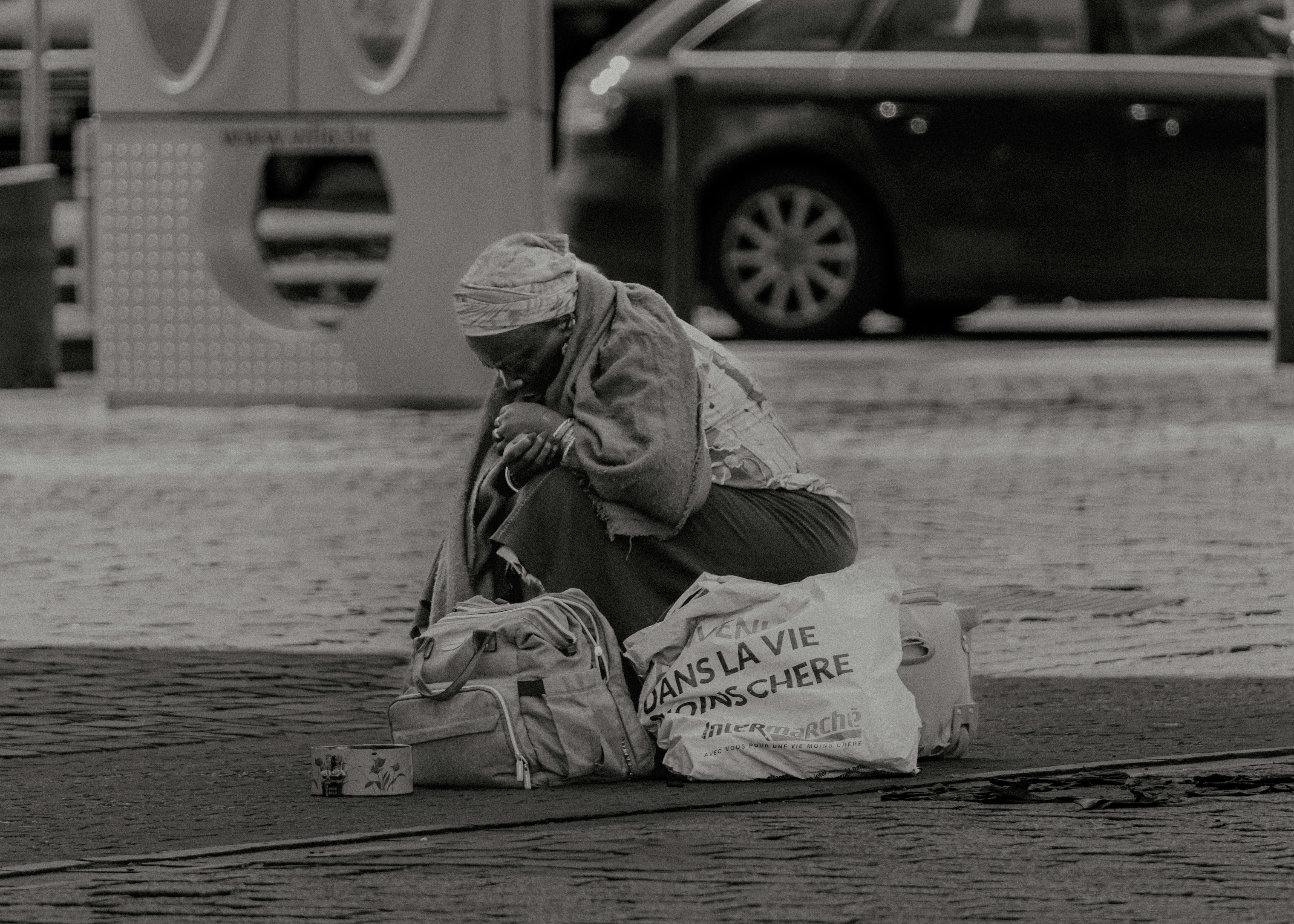 Una persona anziana è seduta in una strada cittadina con le borse.