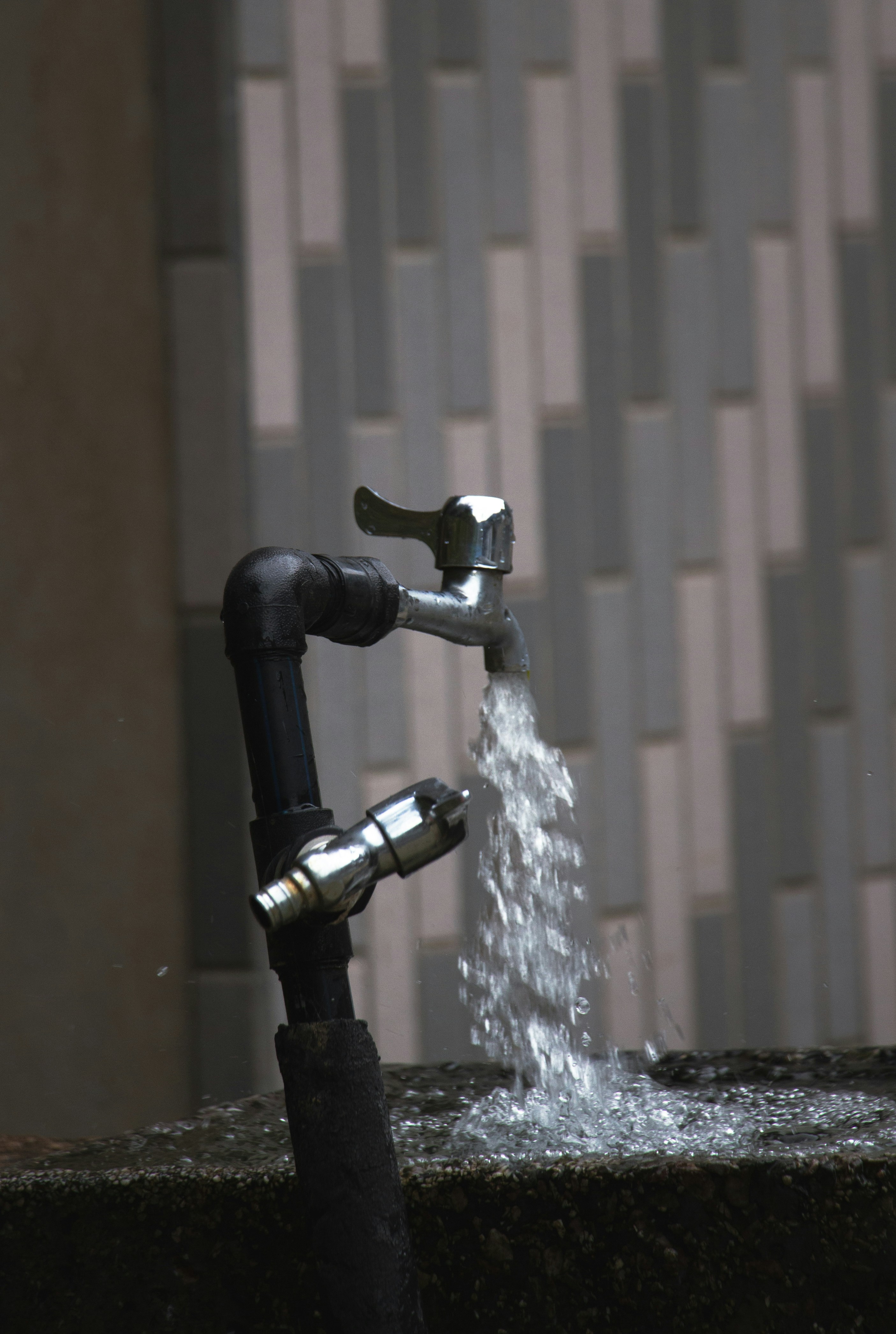 Water flowing from metal faucet attached to outdoor black pipes