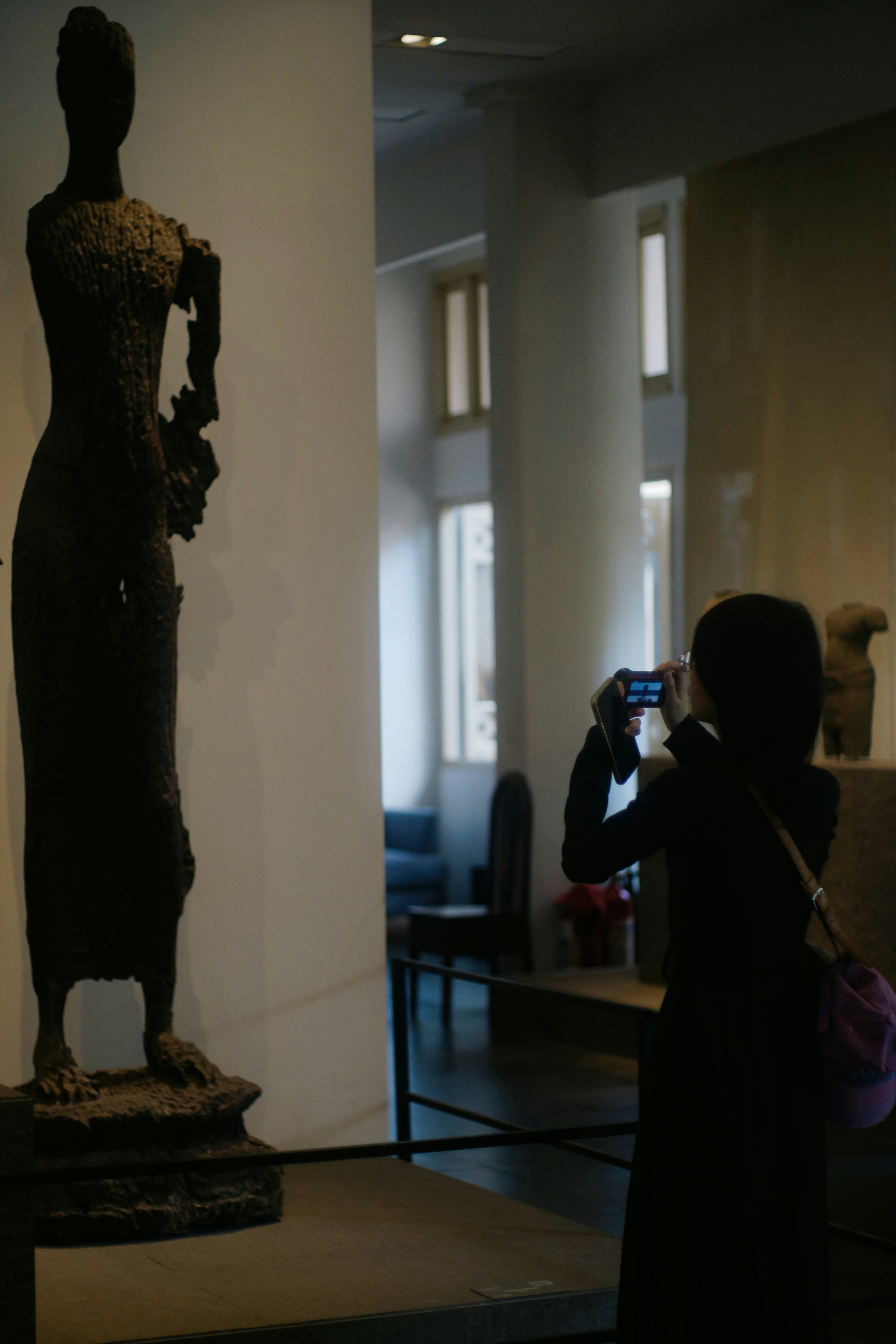 A person photographs a tall, ancient statue in a museum.