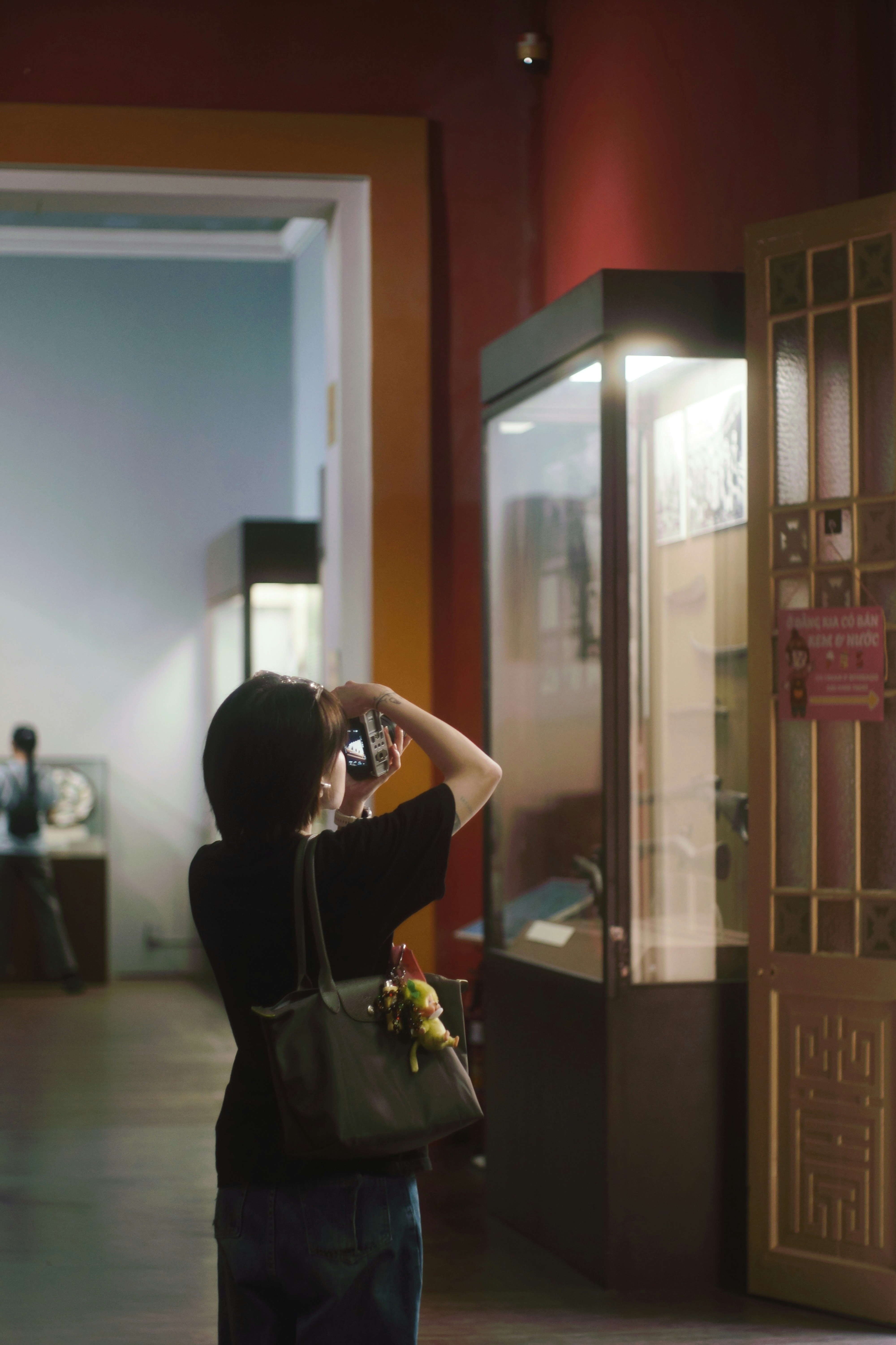 A woman photographs an exhibit in a dimly lit museum.