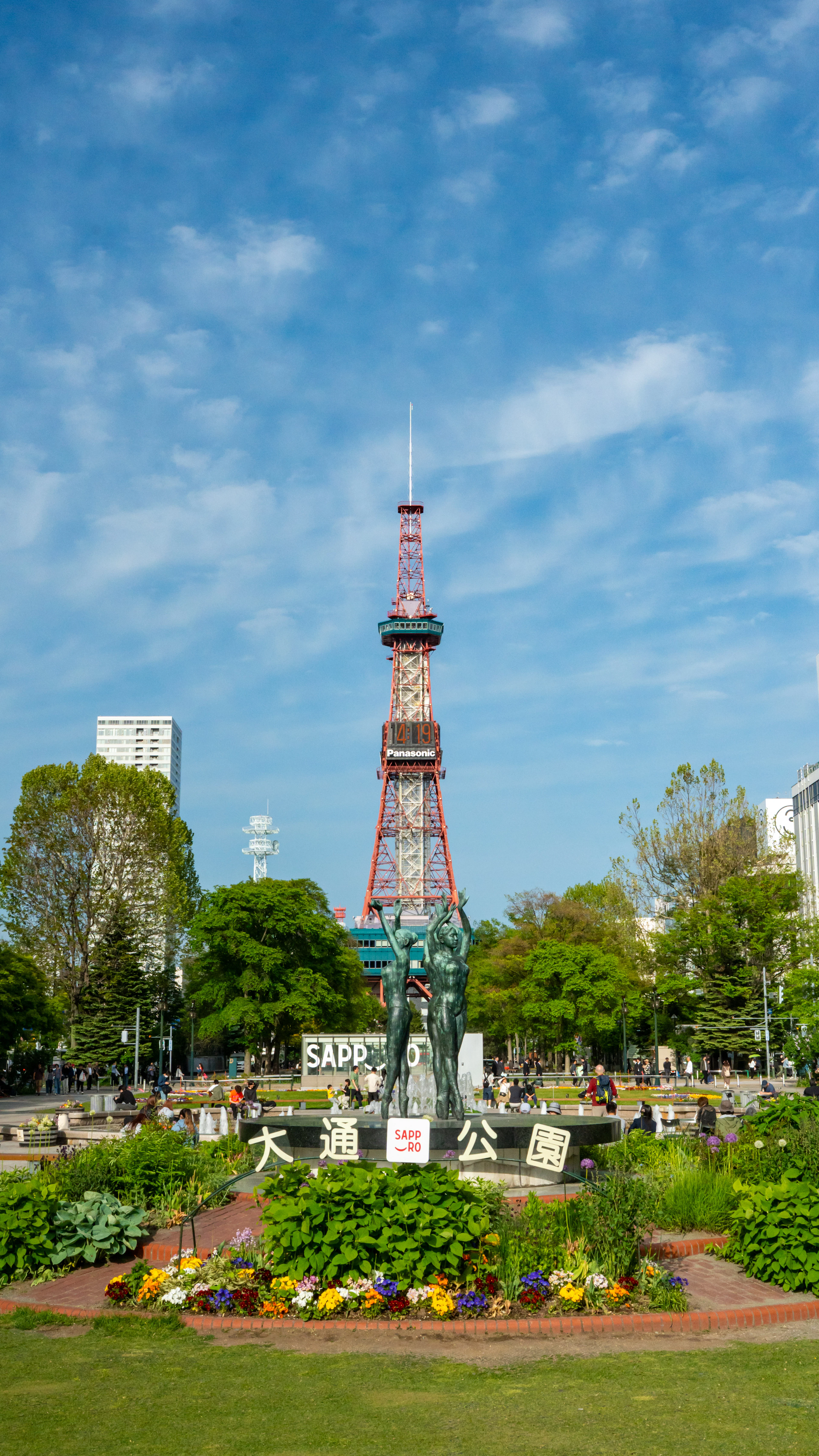 The Sapporo TV Tower rising over the flower beds and fountain plaza of Odori Park under a blue sky
